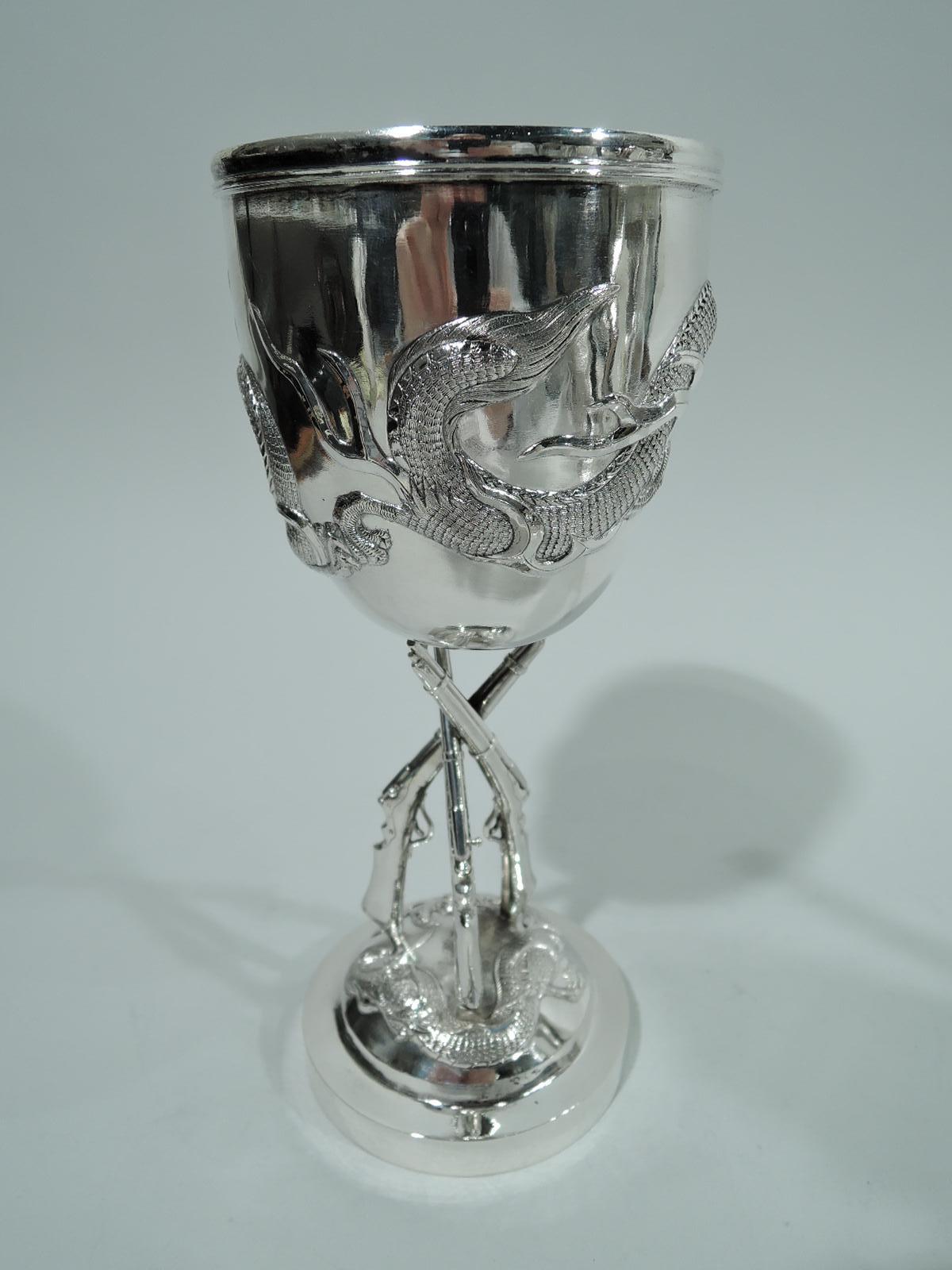 Turn-of-the-century Chinese silver goblet. Ovoid bowl with horned and scaly wraparound dragon in relief, and applied circular frame (vacant). Bowl rests on 3-gun shaft in turn mounted to domed foot with second dragon. An unusual design evocative of