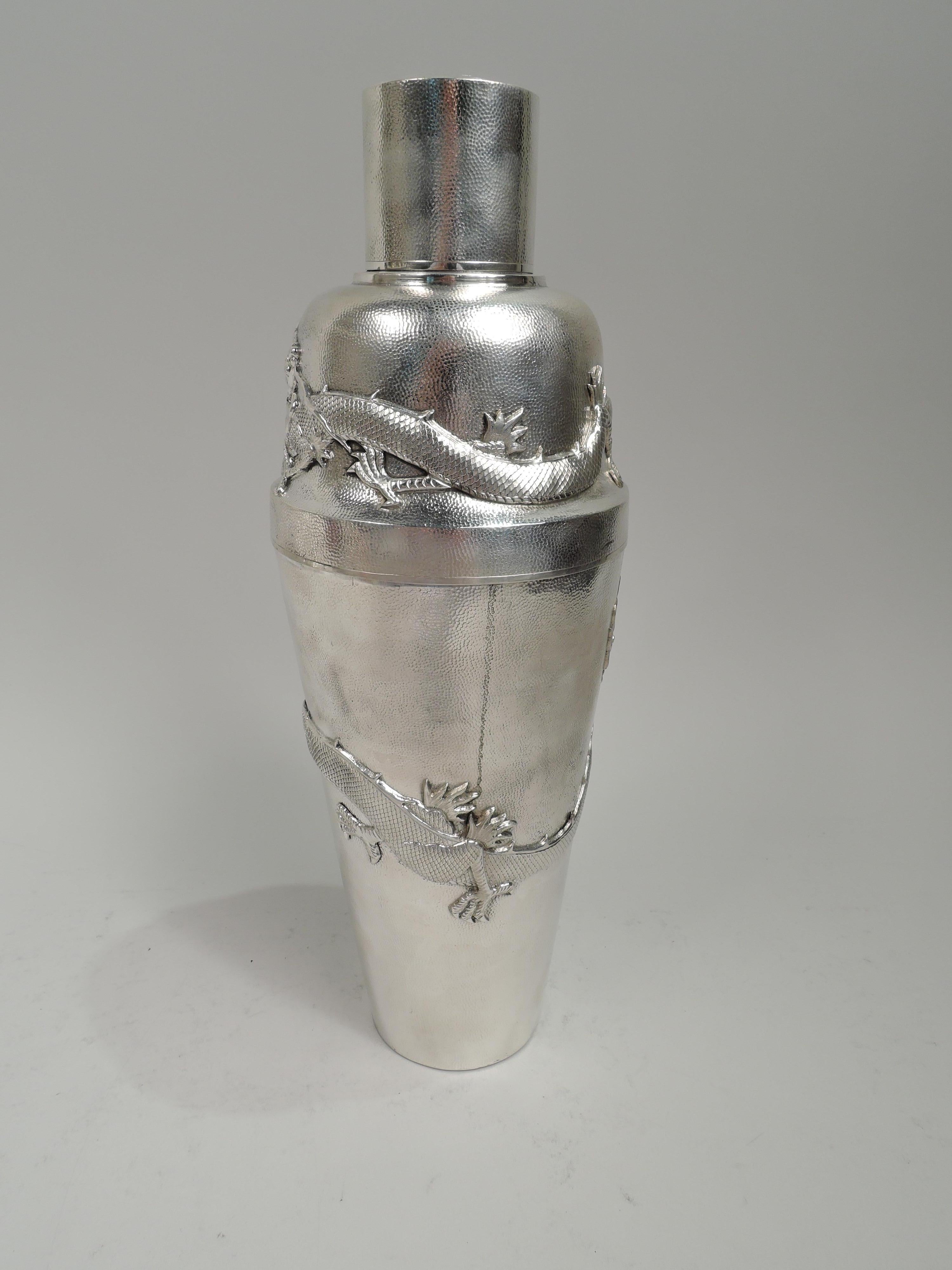 Chinese silver firewater cocktail shaker, ca 1910. Tapering bowl and detachable top with curved shoulder and inset neck with built-in strainer and snug-fitting cap. Stippled ground applied with wraparound dragons: Horned and scaly beasts with sharp