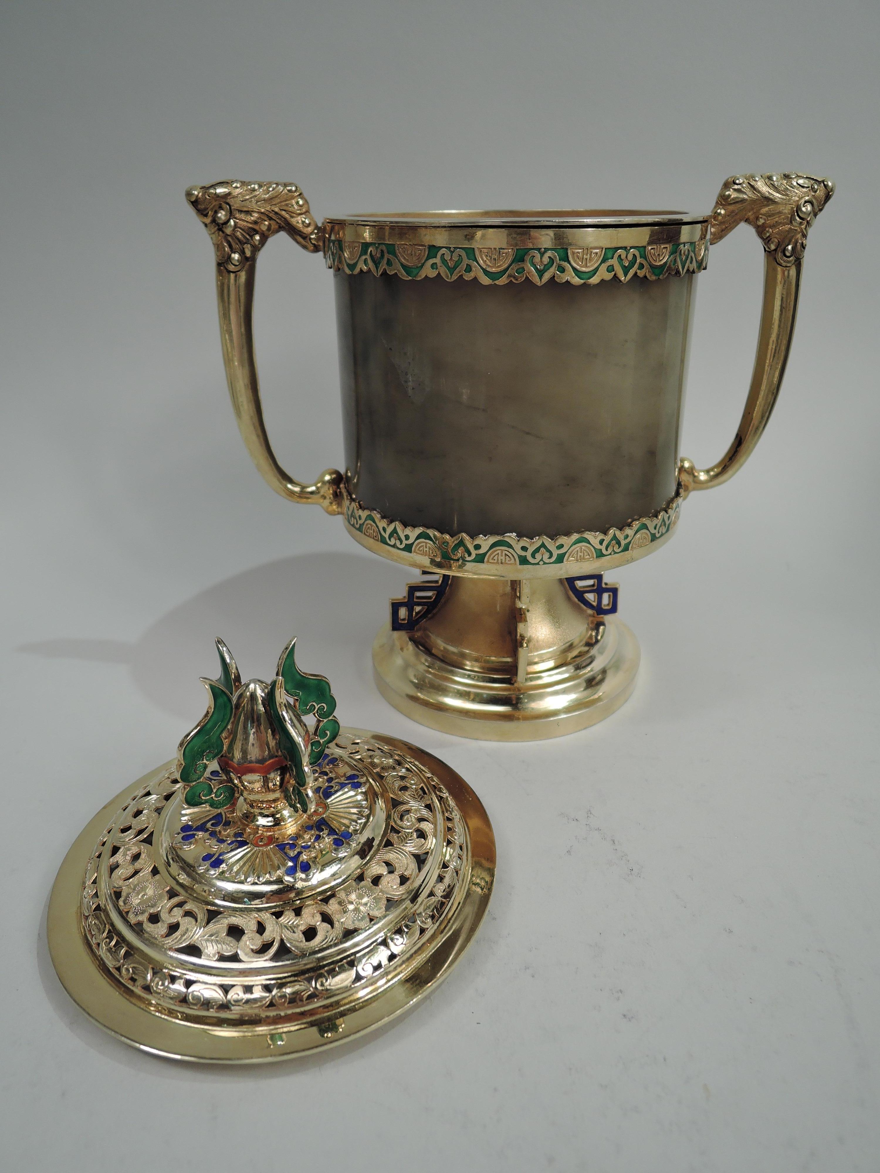 Chinese silver censer, circa 1910. Drum-form agate body set in silver gilt mounts with scrollwork and lunettes. Leaf-capped side bracket handles. Upward tapering support and stepped foot with fretwork brackets. Cover raised with pierced scrollwork