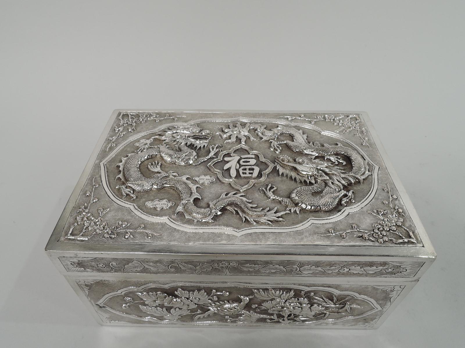 Vietnamese silver box, late 19th century. Rectangular with straight sides. Cover flat and hinged. Box sides have embossed blossoming branches, bamboo, and bird; engraved leaves and flowers at corners. Cover top has embossed slithering, scaly dragons