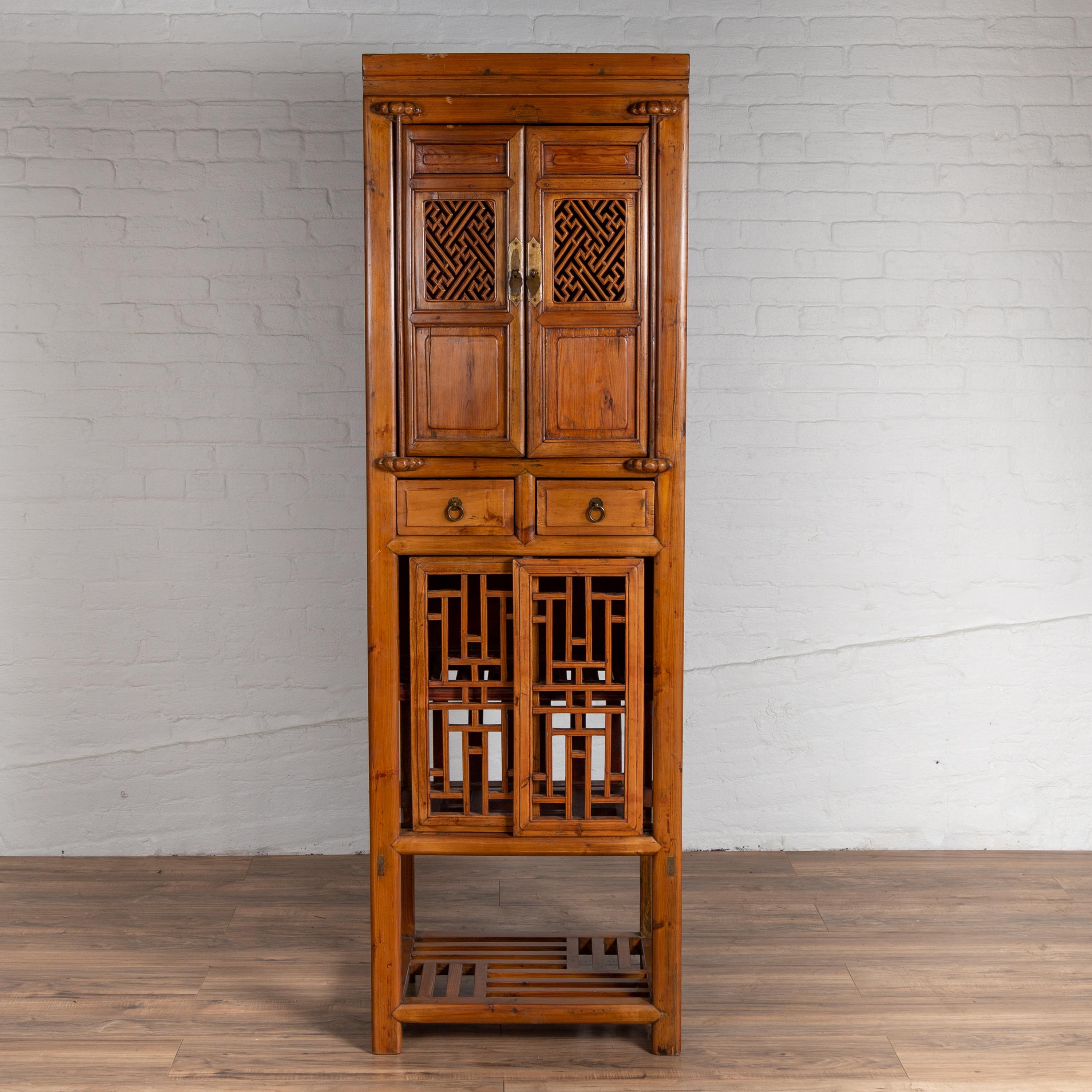 An antique Chinese tall kitchen cabinet from the early 20th century, with open fretwork door panels, sliding doors and cracked ice shelf. Found in Taiwan, this slender Chinese cabinet features a molded cornice sitting above double doors, accented