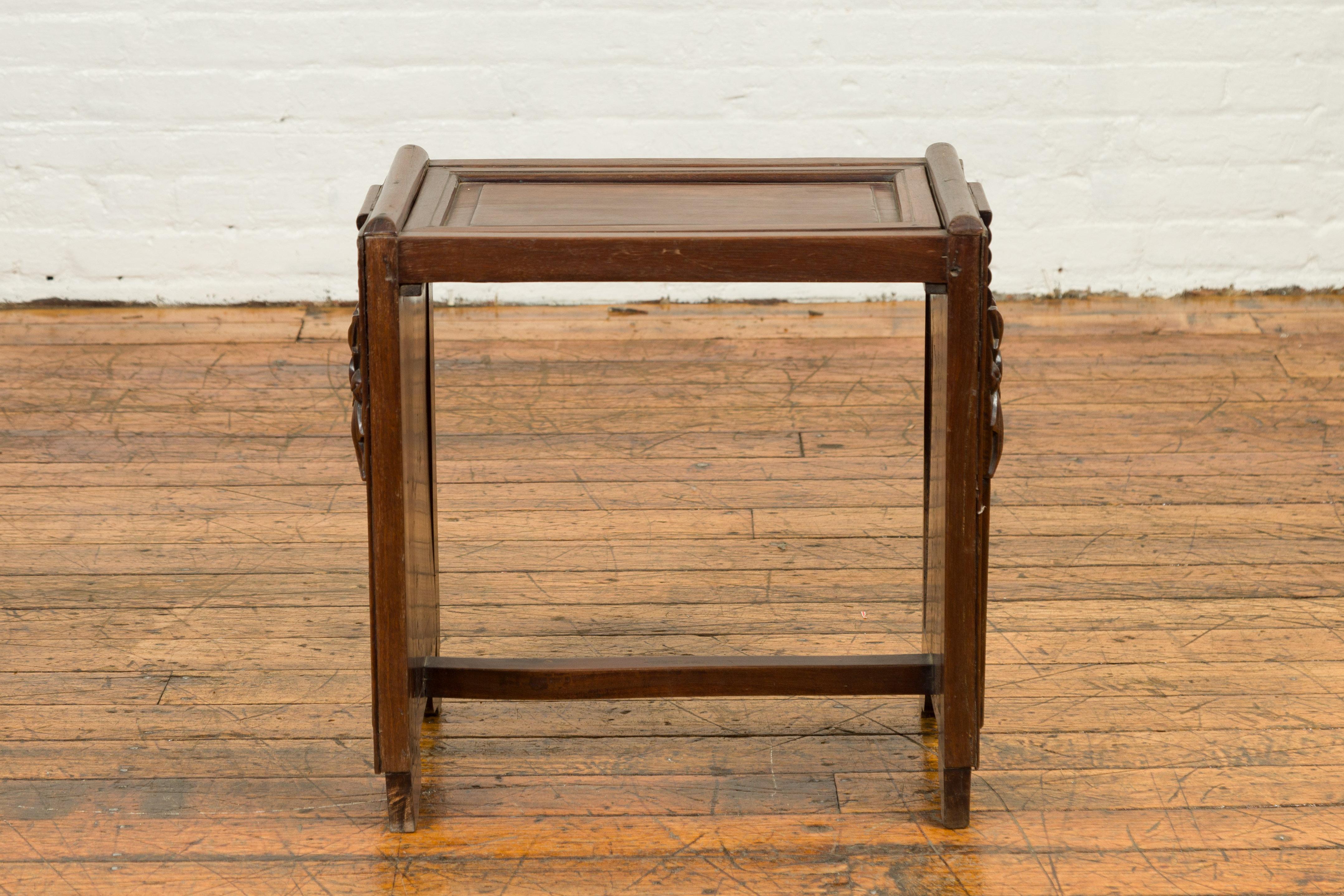 A Chinese antique side table from the early 20th century, with removable top, carved floral motifs and unusual shape. Created in China during the early years of the 20th century, this wooden side table features a rectangular removable top sitting