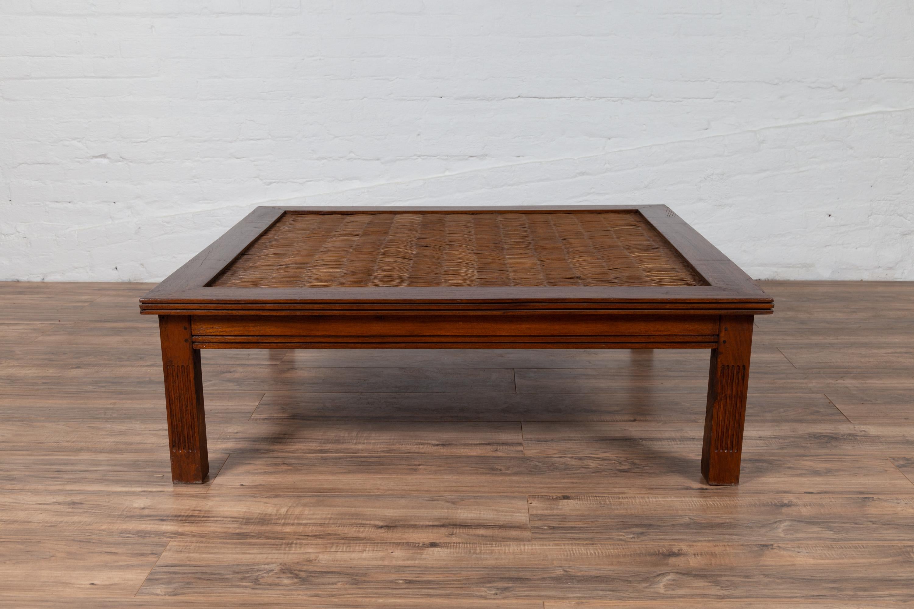 An antique Chinese square-shaped elmwood coffee table from the early 20th century, with handmade rattan inset and fluted motifs. Born in China during the early years of the 20th century, this charming elm coffee table features a rectangular top,