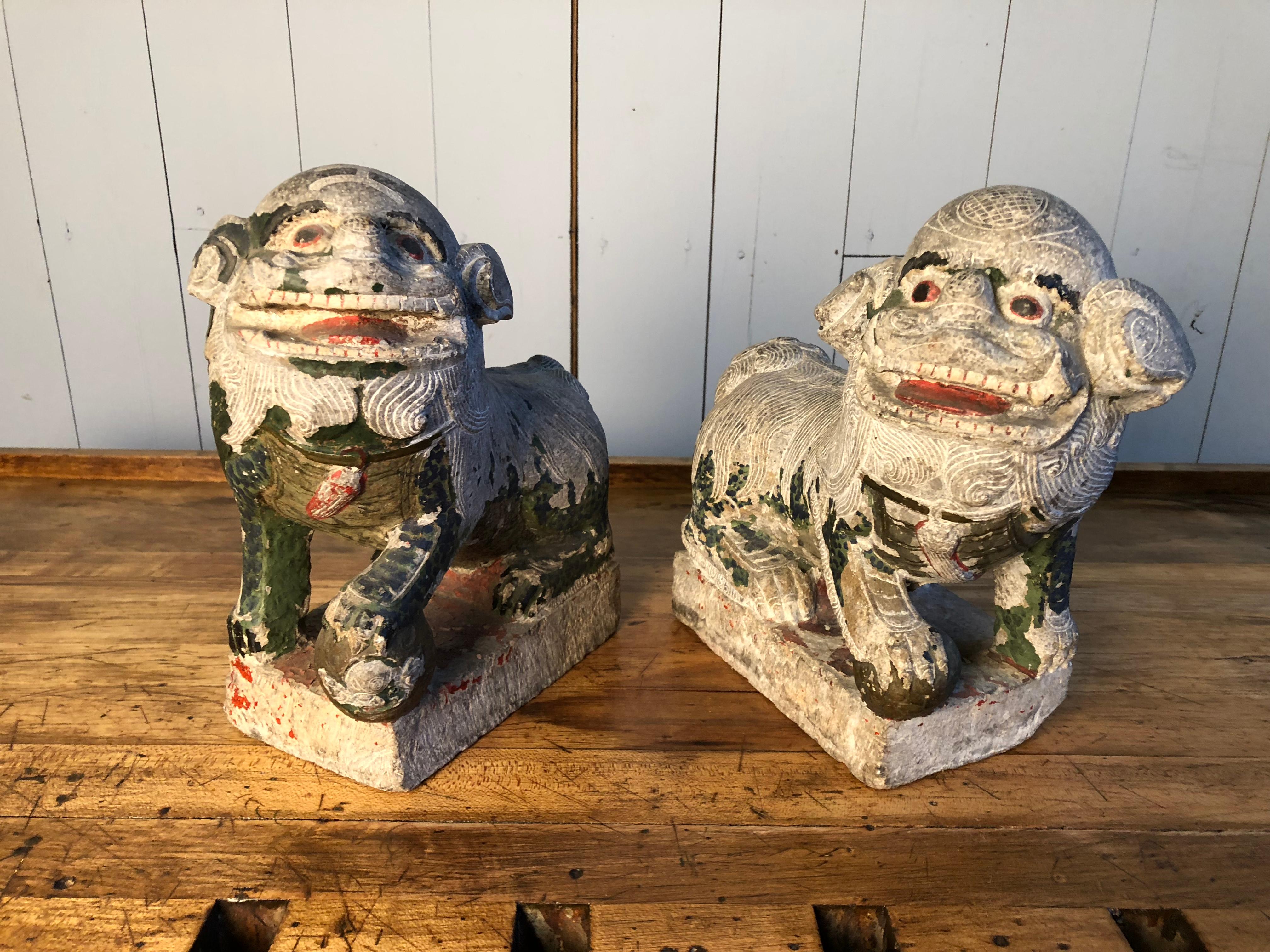 A pair of carved stone Foo Dogs with traces of polychrome painted finish, 19th Century or earlier. Each seated figure with a front paw resting on a ball, facing opposite directions.