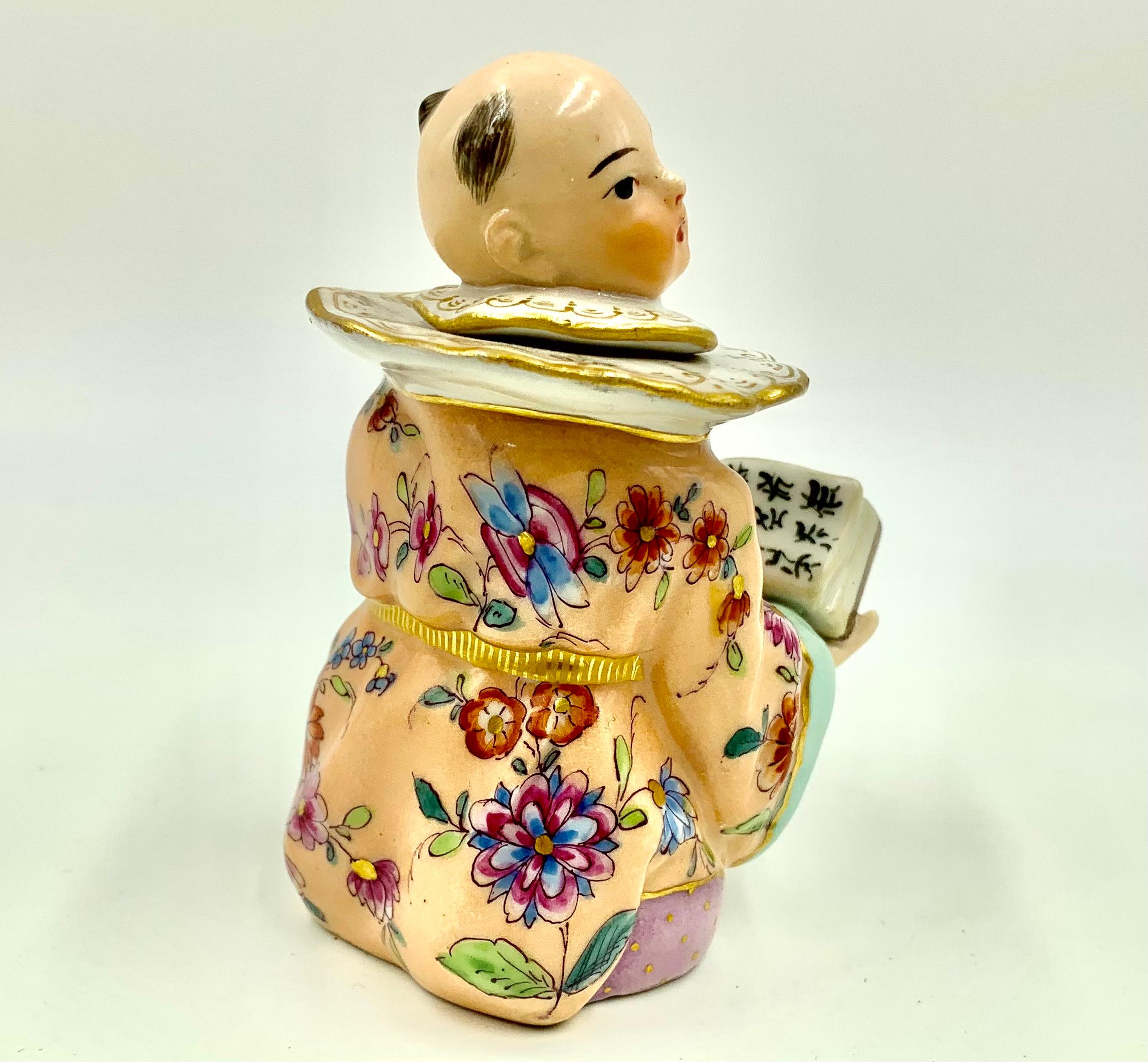 Rare KPM porcelain figural inkwell depicting a Chinaman in a wonderfully ornate traditional robe of pale apricot decorated in a flowing floral pattern of garlands of peonies, Chinese roses, camellia, hibiscus and lotus, topped with prominent gold