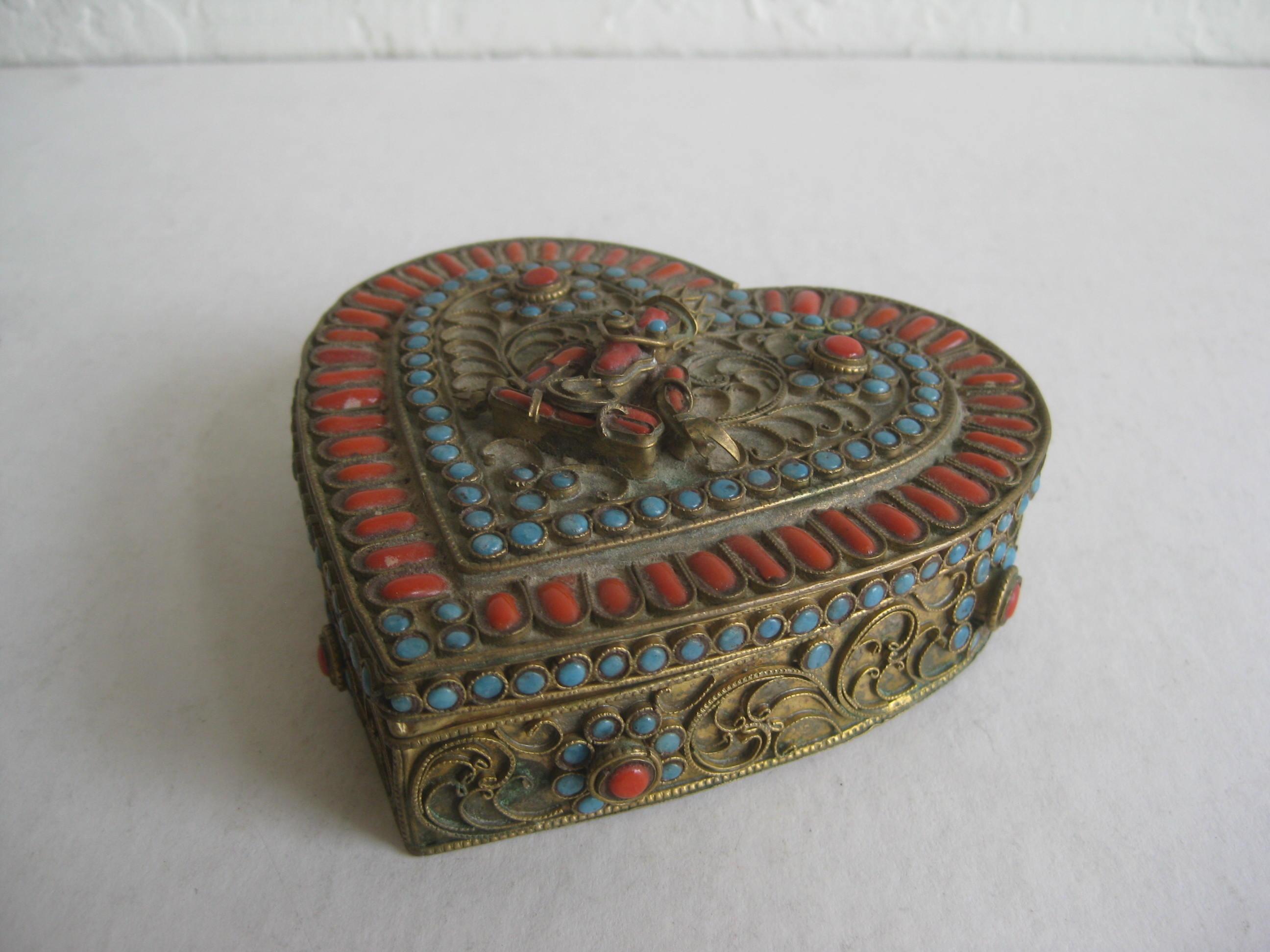 A beautiful Chinese-Tibetan brass heart shaped box with turquoise and coral glass inlay pieces. Great filigree design with a buddha figurine on the top. Has a wonderful patina. In good shape with age appropriate wear. Has no missing pieces. Opens