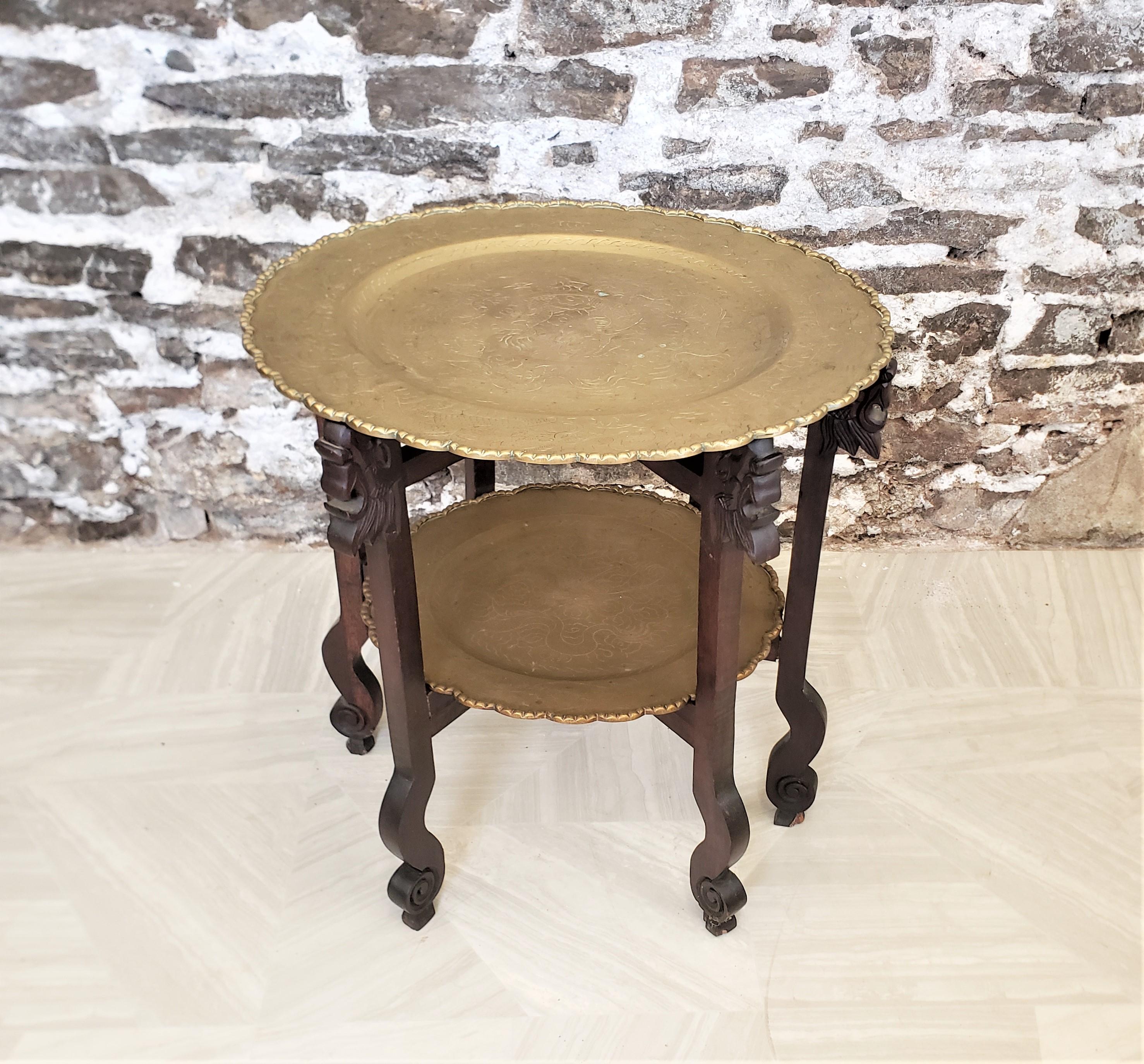 This antique tray table is unsigned, but presumed to have originate from China and date to approximately 1920 and done in a period Chinese Export style. The table set is composed of two brass trays with pie crust edges and engraved tops with a hand