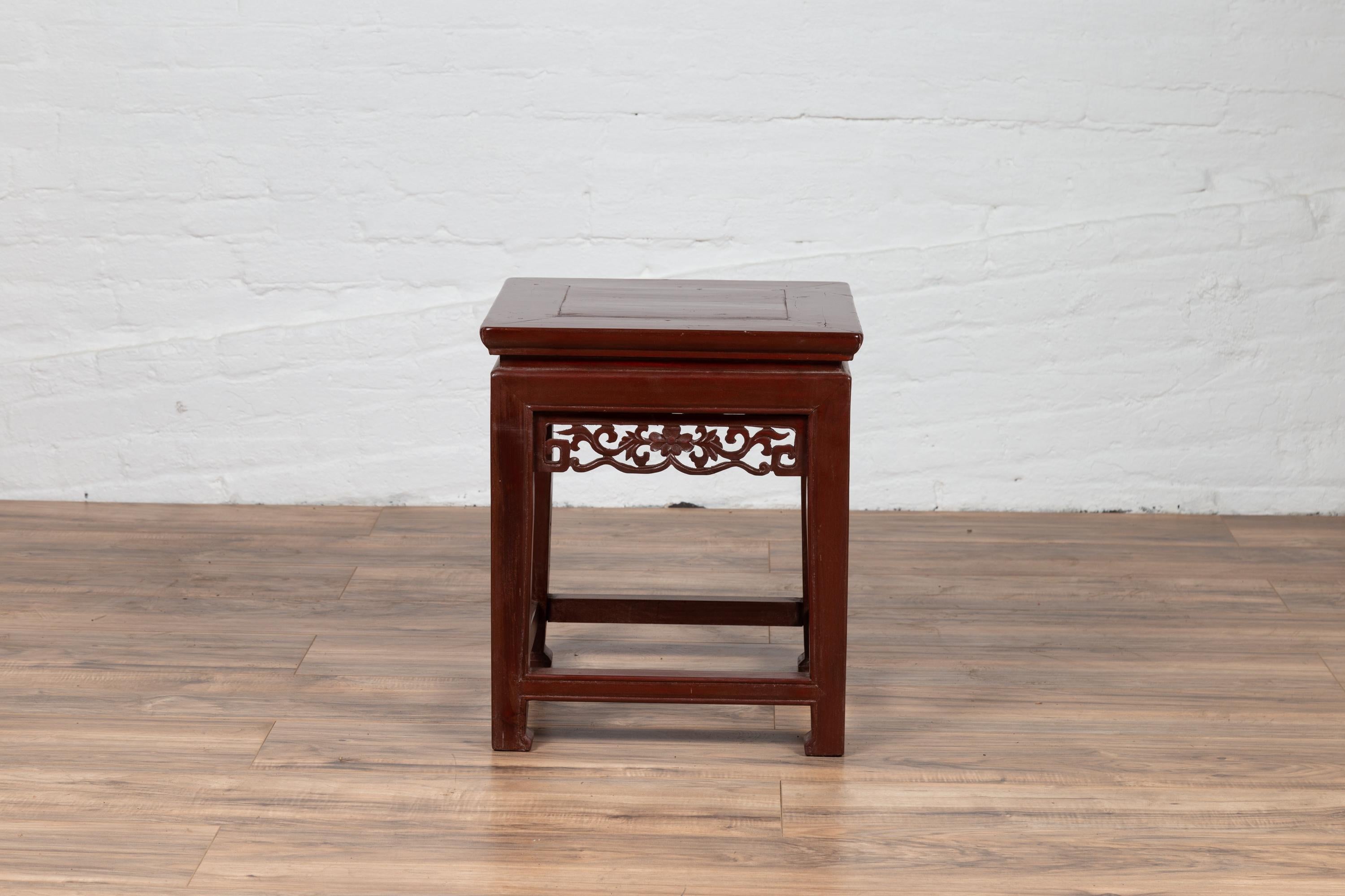 A Chinese antique waisted wooden stool from the early 20th century, with dark red patina and carved apron. Born in China during the early years of the 20th century, this Chinese wooden stool presents a perfect contrast between the gentle linearity