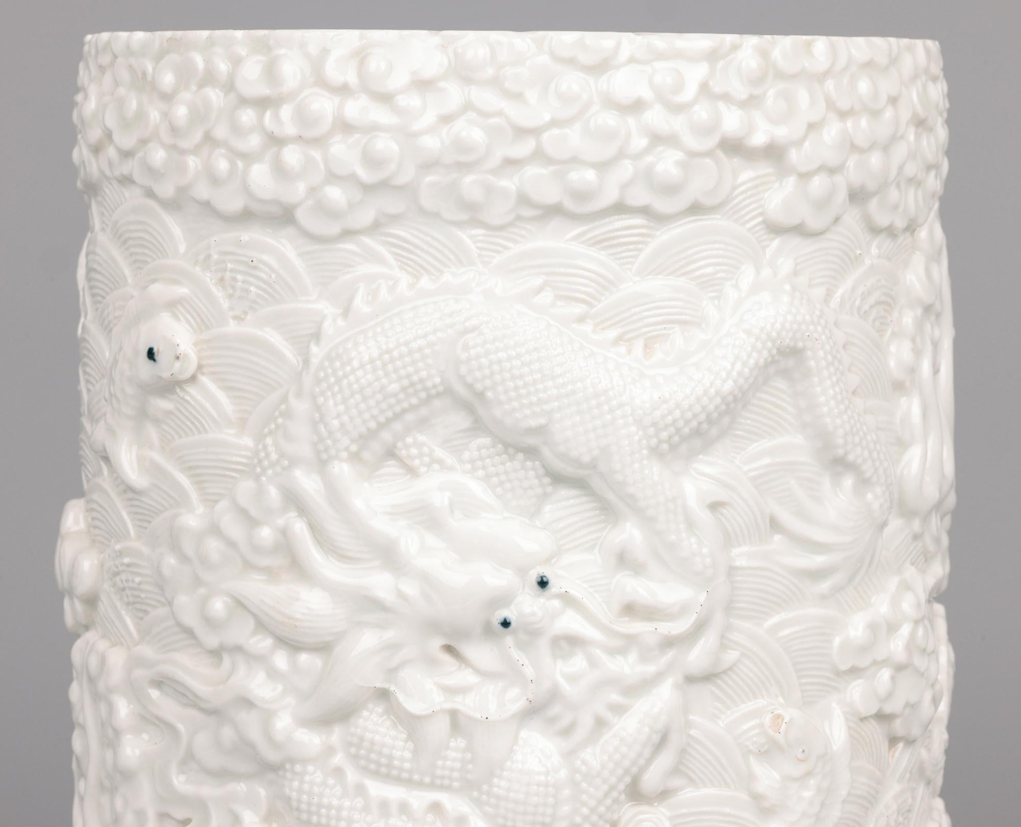 Superbe pot à pinceau ancien en porcelaine chinoise à glaçure blanche de forme cylindrique finement moulée en relief avec des dragons se battant en duel au-dessus de vagues avec des poissons sautant et d'autres décorations moulées avec les yeux