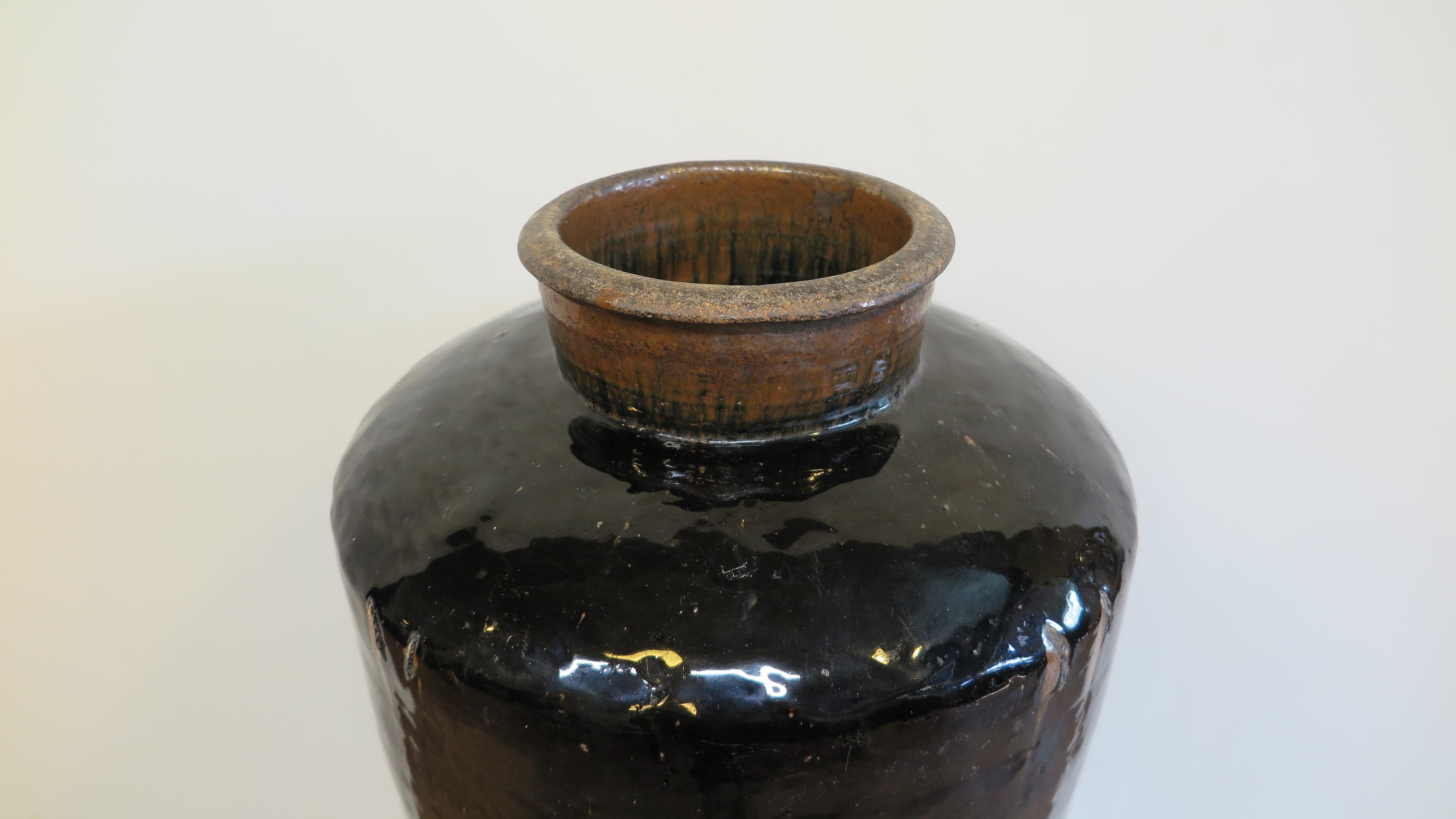 Chinese earthen ware storage jar. 19th century stoneware large black glaze storage jar. Excellent shape having wide raised mouth opening with flared rim spout on domed edged top tapering to narrowed bottom. The black glaze has significant depth