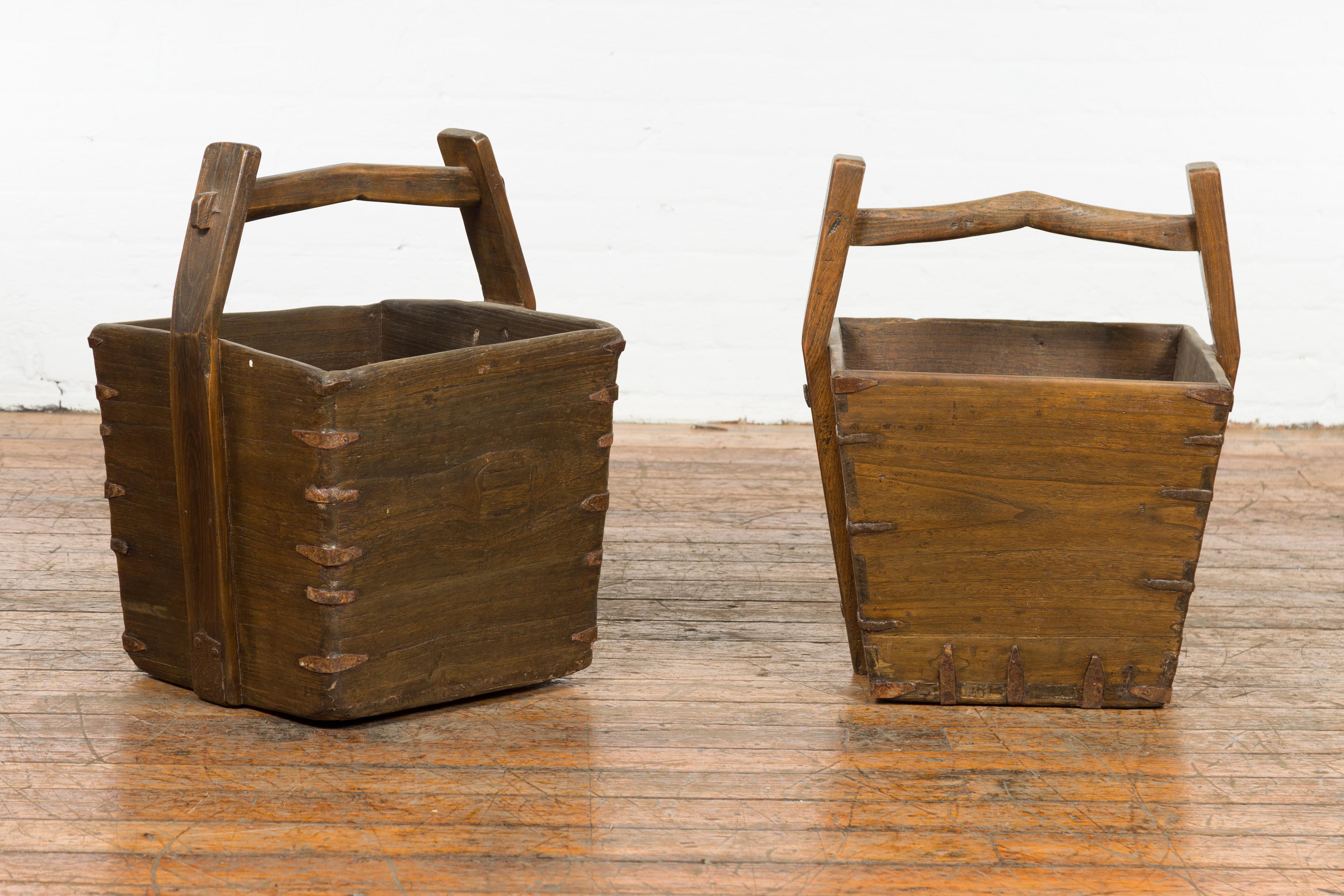 Two rustic Chinese Qing Dynasty period wood grain baskets from the 19th century, with large carrying handles and metal braces. These are priced and sold individually. We also have several baskets coming in different sizes and with different designs.