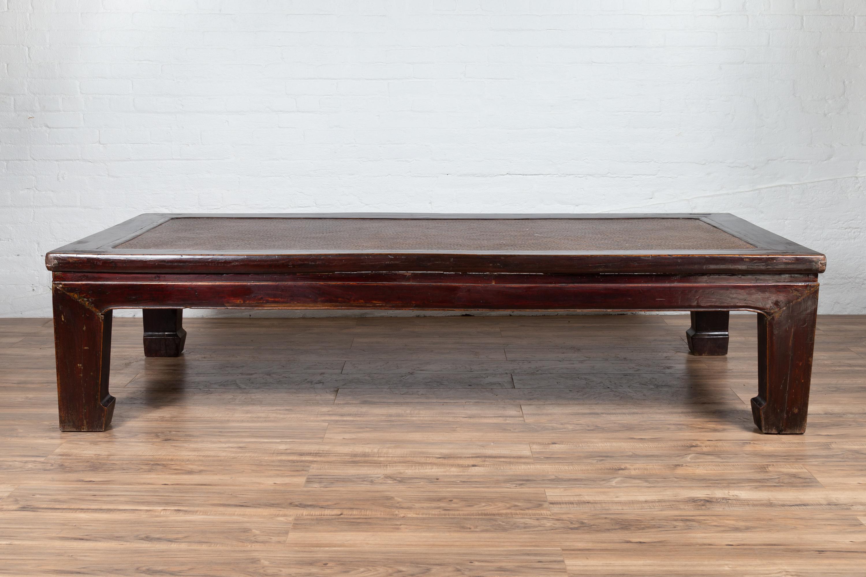 An antique Chinese wooden coffee table from the early 20th century, with dark burgundy patina, woven rattan top and sturdy horse hoofed legs. Born in China during the early years of the 20th century, this charming coffee table, originally created to