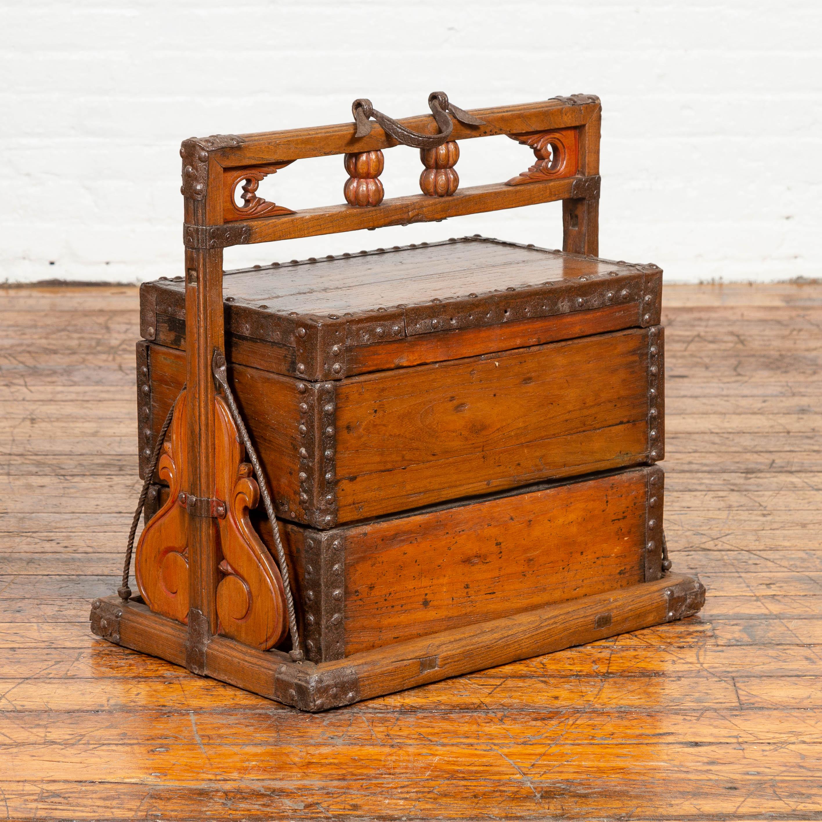 An antique Chinese wooden tiered carrying wedding treasure box from the early 20th century, with large volutes, handle and nailheads. Born in China during the early years of the 20th century, this wedding box features a linear silhouette, accented