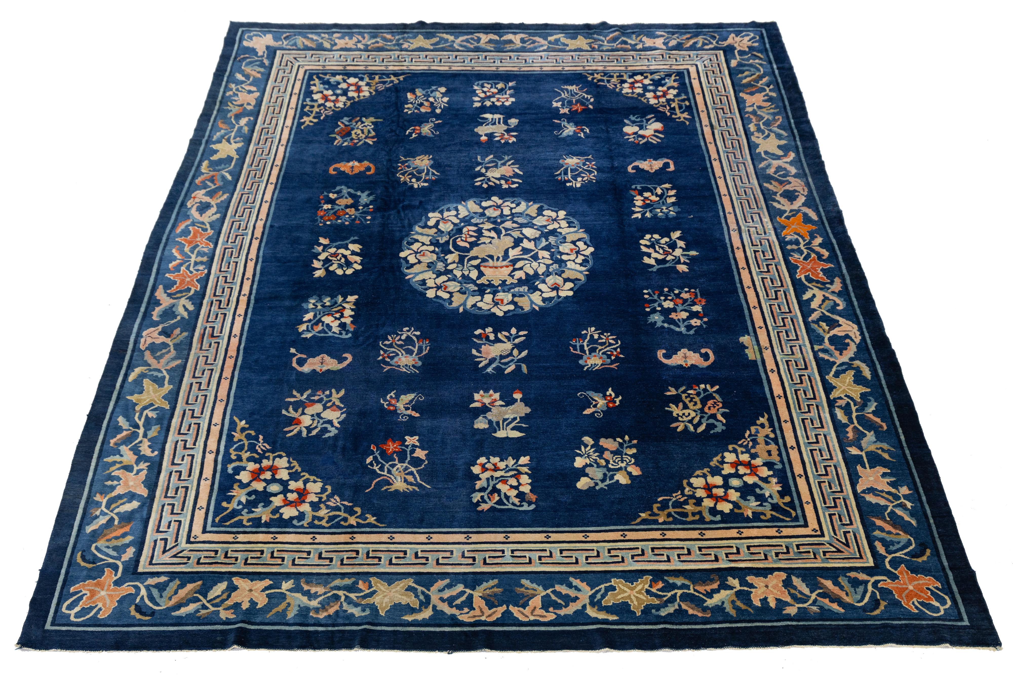 Antique Chinese wool rug, handknotted with a rich blue field and central floral medallion. Features symbolic motifs in a grid layout and a geometric vine border in soft beige, orange, and green. A refined decorative piece showcasing early