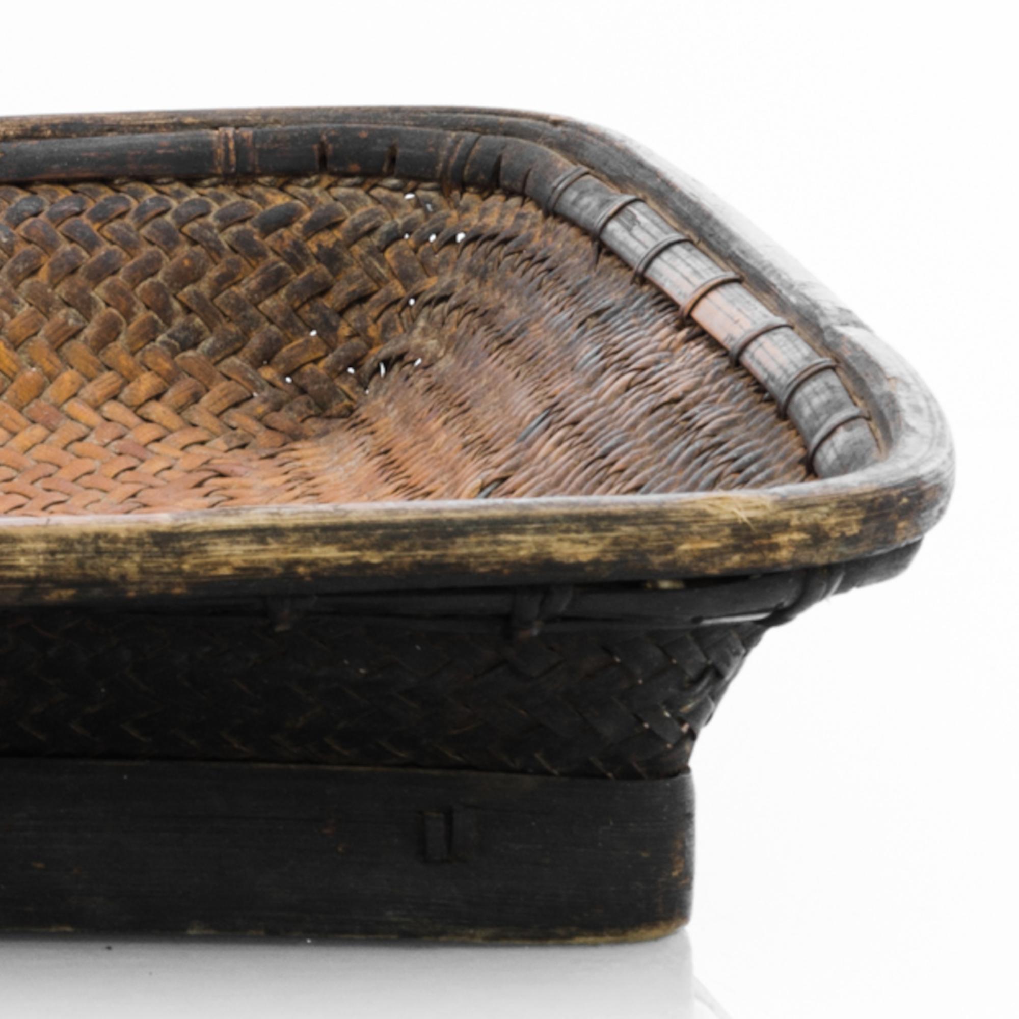 This wooden basket was made in China, circa 1900. Recalling simple techniques and natural materials, carefully refined with a dark color and revealing the rustic touch of time. Shallow, with a rectangular base, this piece could have been used as a