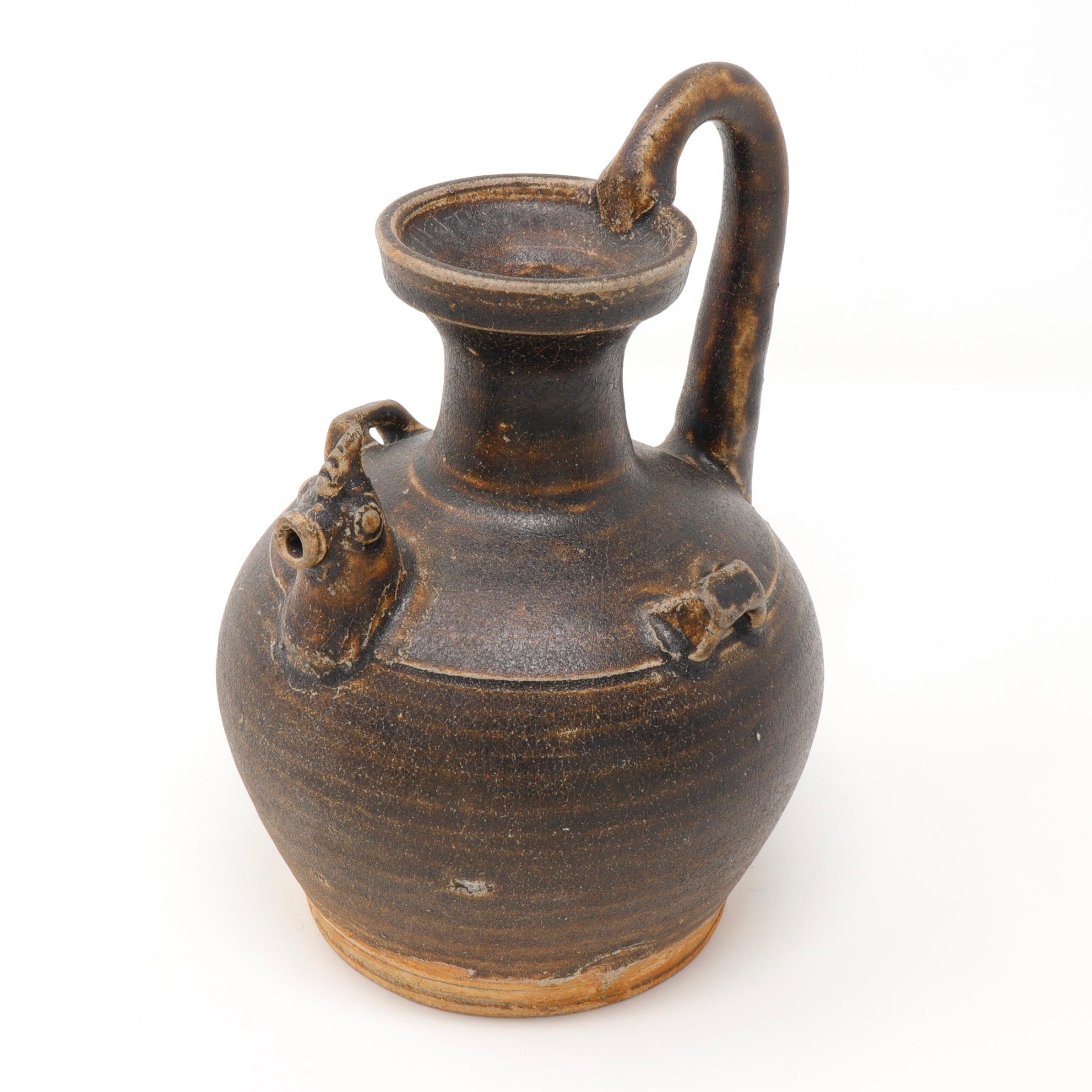 A globular stoneware body that is well potted with a cup shaped mouth supported on a narrow tall neck. The characteristic chicken head form serves as the spout. The handle is pulled and applied from the shoulder to the mouth. Another characteristic