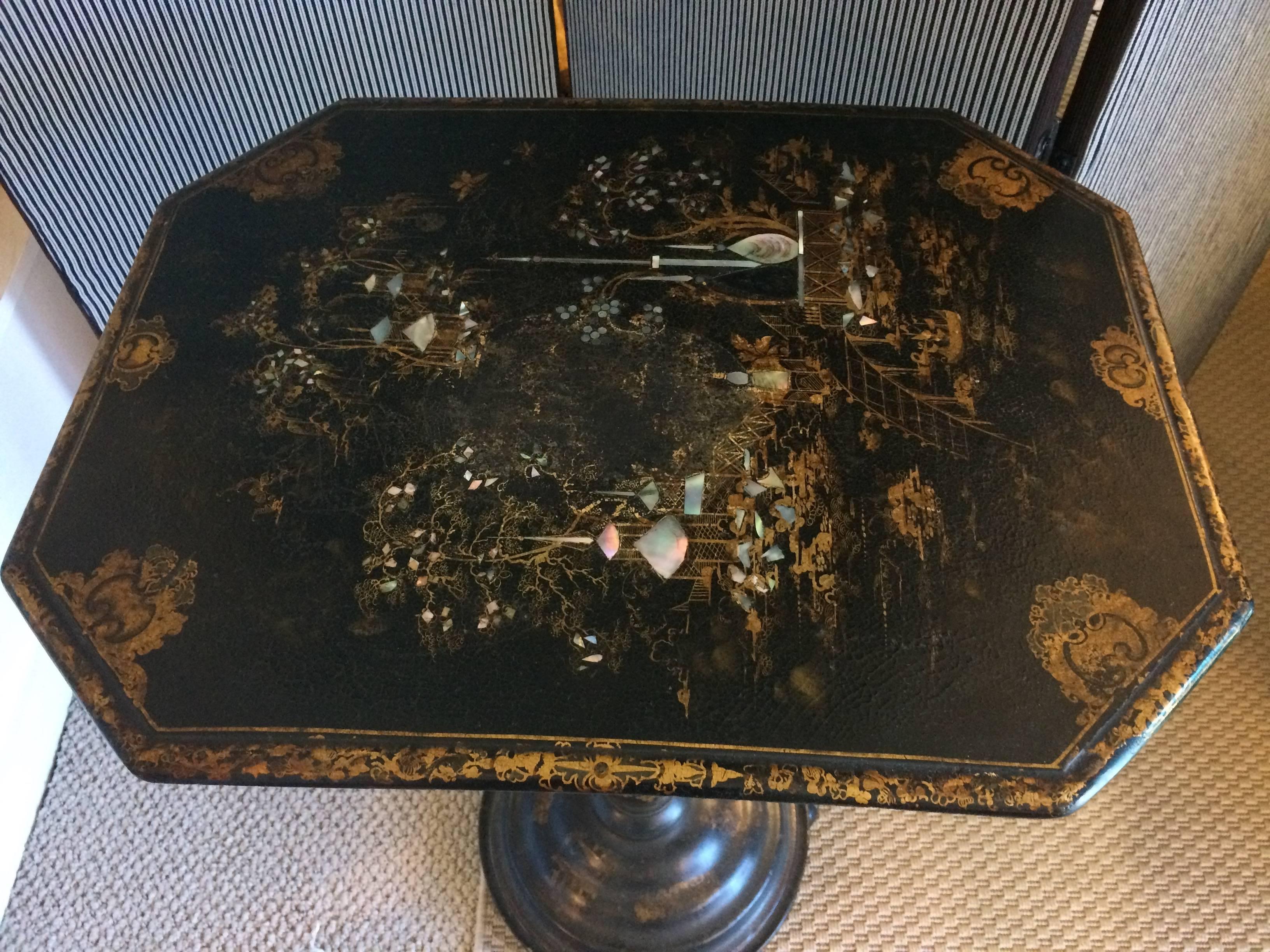 Classically elegant chinoiserie style side table having an octagonal shaped top with meticulous mother-of-pearl inlay and gold painted landscape scene, resting on a single pedestal and round base with feet.