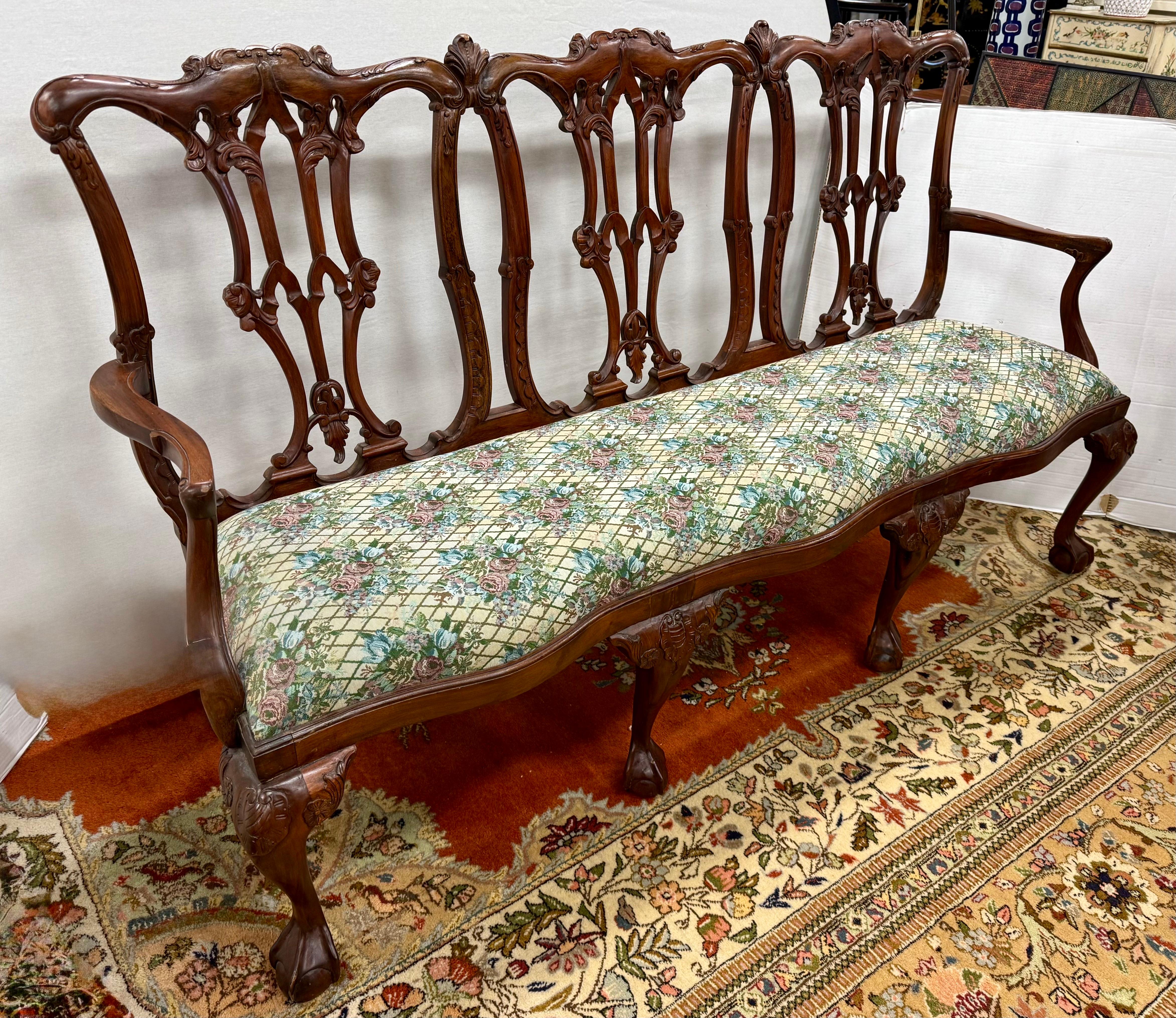 Exquisite antique Chippendale three seat mahogany bench showcases high quality craftsmanship, featuring intricately carved back splats and graceful scrolled arms. The rich mahogany wood boasts a warm, lustrous finish, beautifully complemented by