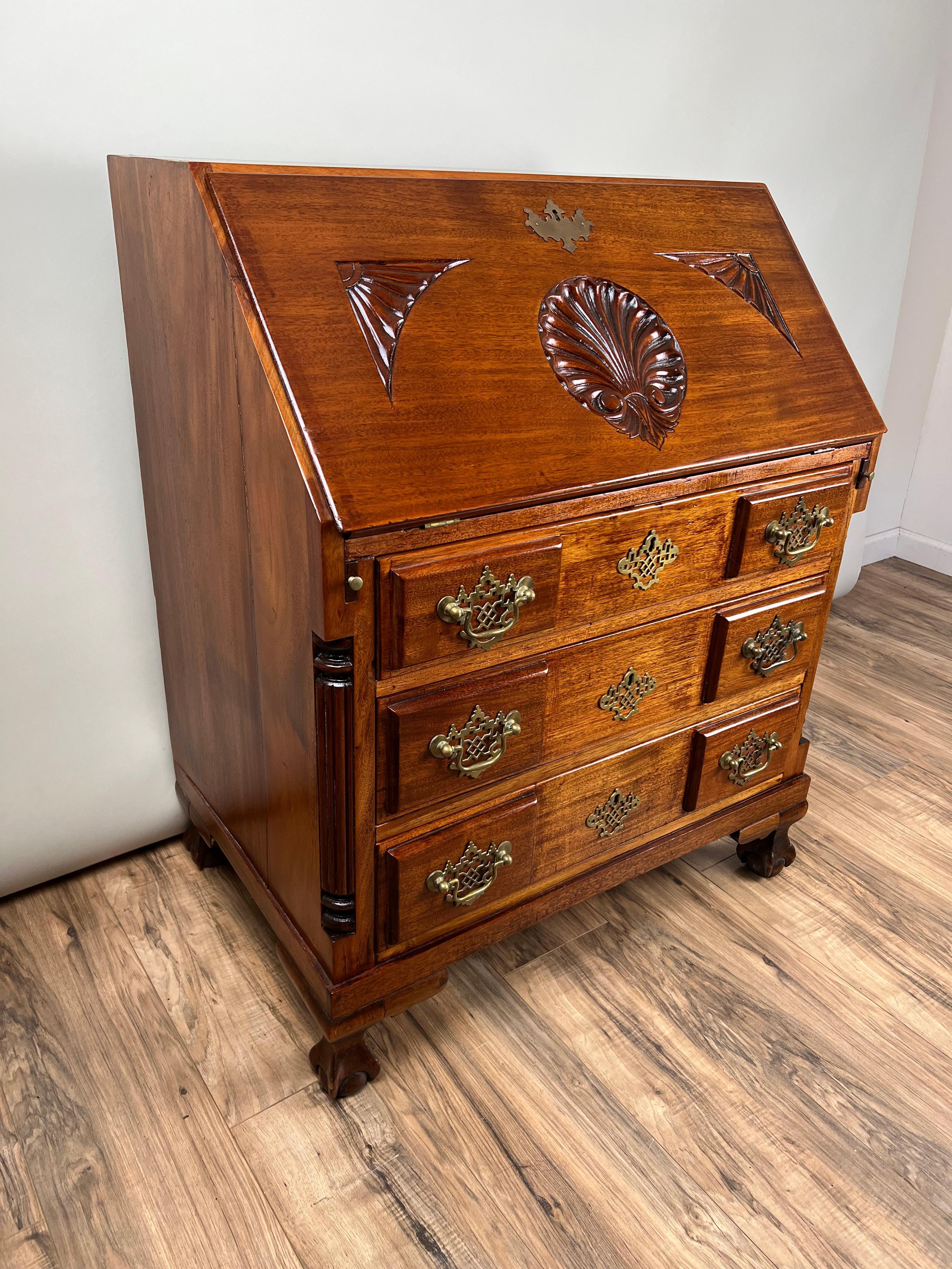 Preciosa secretaria de principios del siglo XX, de estilo Chippendale, probablemente fabricada hacia 1910. Esta majestuosa pieza está fabricada en rica caoba y presenta una superficie de escritura con frente abatible sobre una clásica disposición de