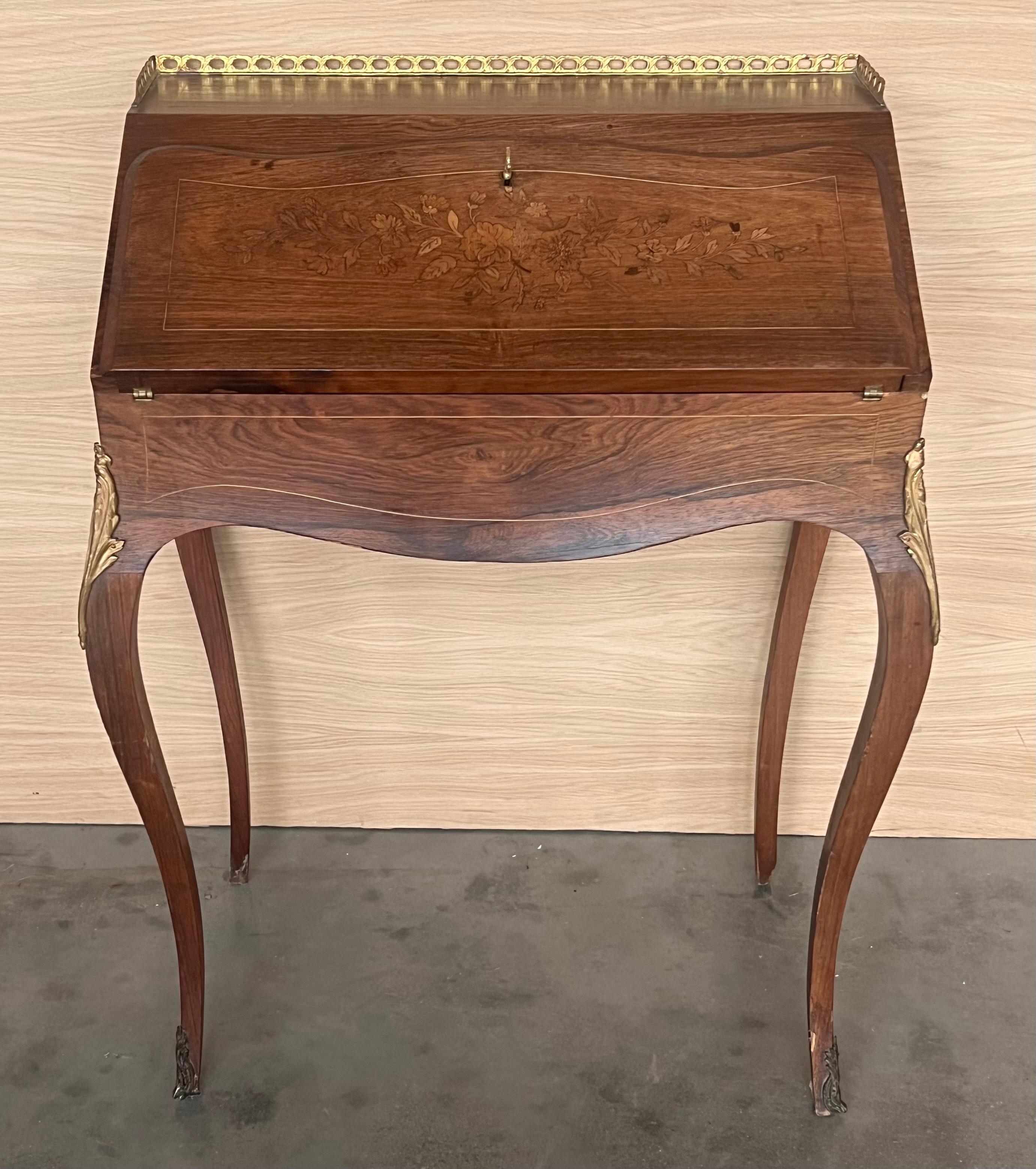 An antique early 20th century ladies' secretary desk. Made from walnut with a maple writing surface. Features a drop front with neoclassical brass hardware over large central drawer with French pulls. Opens to two pigeonholes and an accessory
