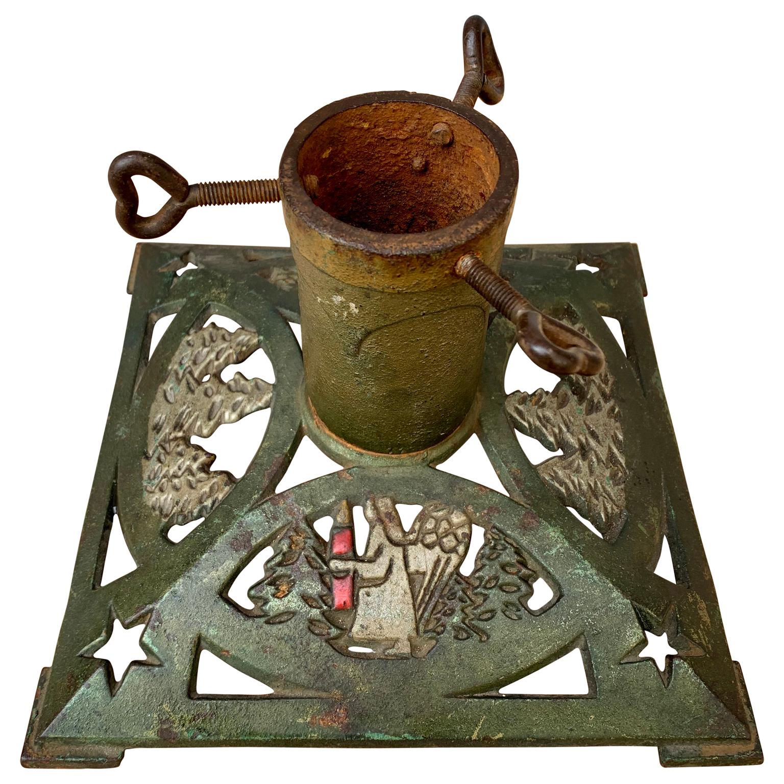 A small square Christmas tree stand in original painted cast iron from circa 1900s. Decorated with snow covered trees and angels carrying a red candle. With the screw to hold the tree in the foot, forged in form of hearts. The inside diameter of the