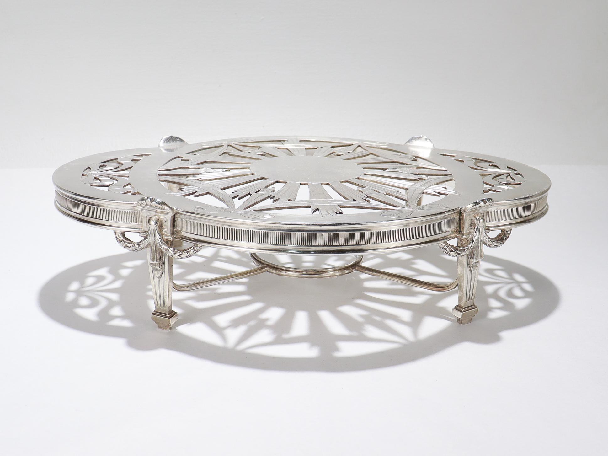 A fine French footed trivet or plateau.

By Christofle.

In silver plate.

With a quatrefoil, lobed top with pierced ribbon work and a sunburst opening supported on 4 tapered Neoclassical legs.

The center with a grill for a burner. (Burner not