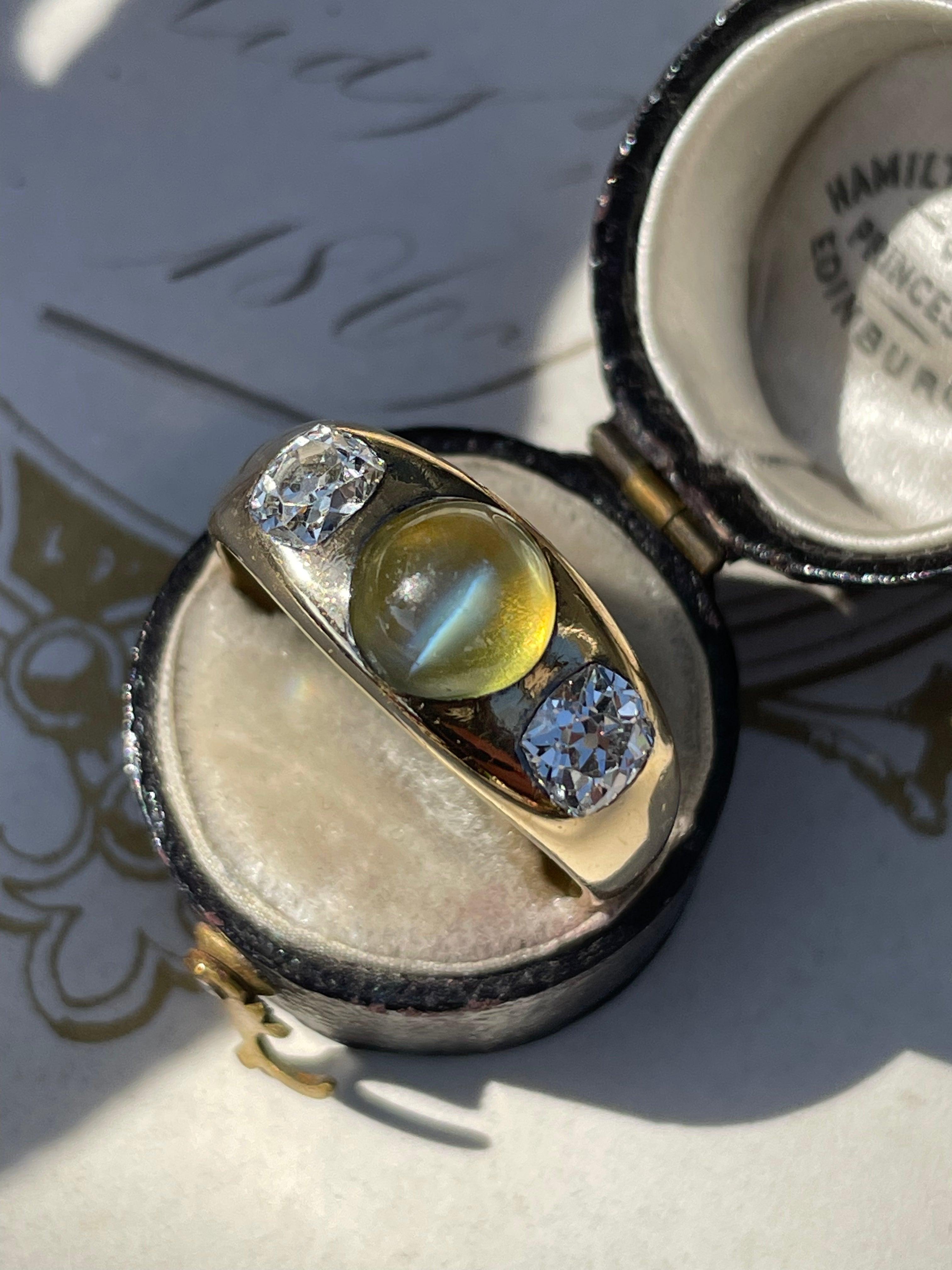 A mesmerizing honey colored cat's eye chrysoberyl, weighing 3 carats, is nestled between a pair of gorgeous old mine-cut diamonds in this exceptional antique ring. The trio is mounted in tapered 14k yellow gold rubover setting with an open back.