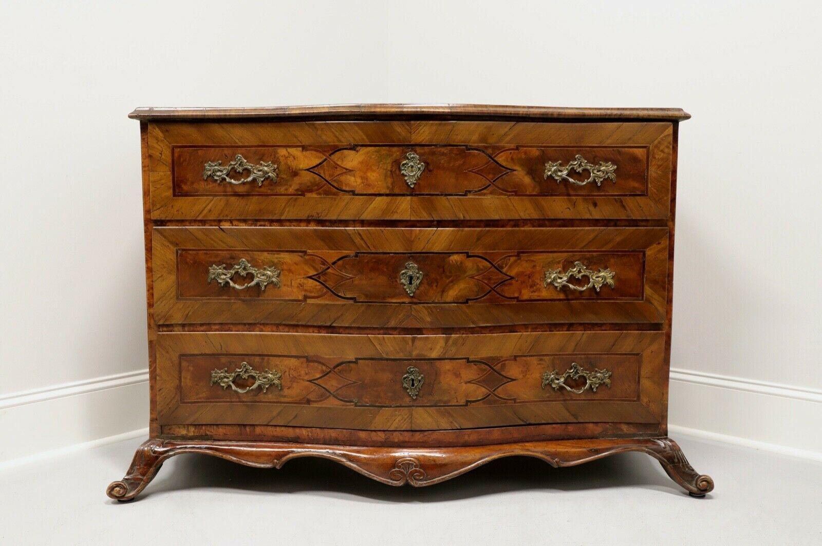 An antique German Baroque style bowfront three-drawer chest, unbranded. Walnut and veneers with brass hardware. Inlaid overall with parquetry and scrollwork inlay all raised on splayed scroll feet. Three dovetail drawers with faux lock plates on two