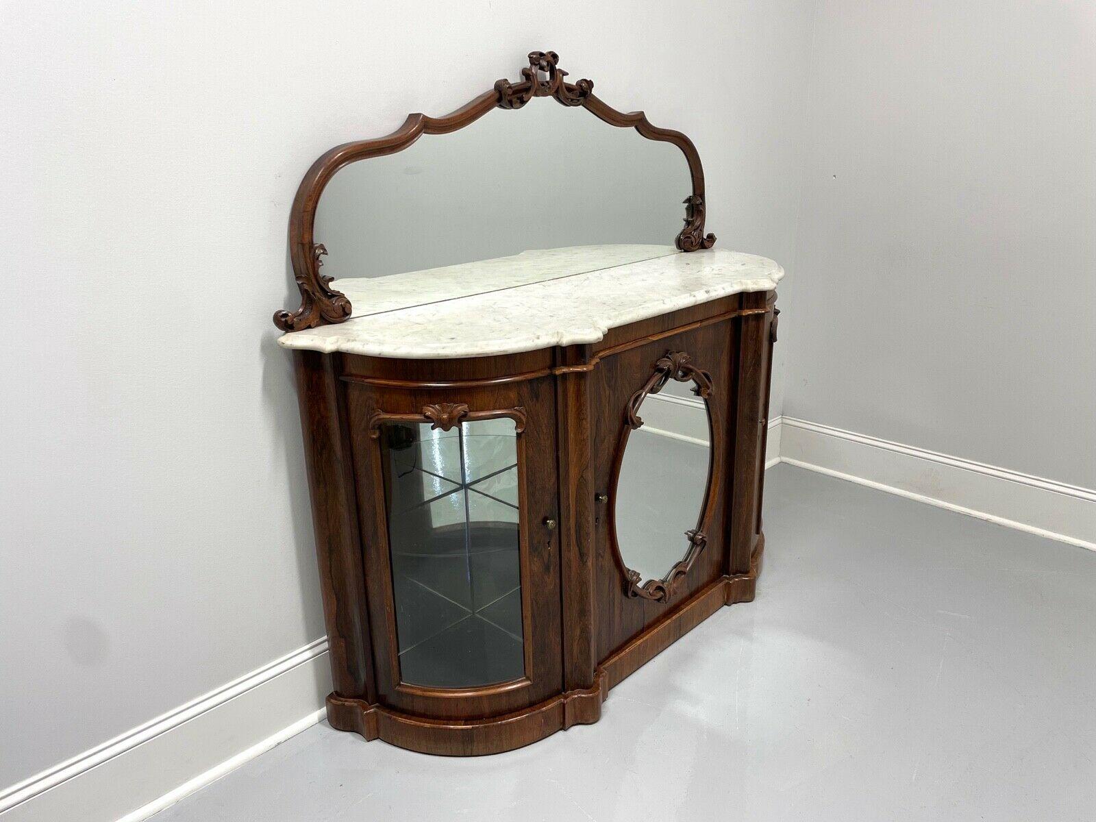 An antique mid-19th century credenza in the Victorian Rococo Revival style, unbranded. Rosewood & rosewood veneers with decoratively carved mirror backsplash, original serpentine shaped white marble top, decorative carvings to center door panel