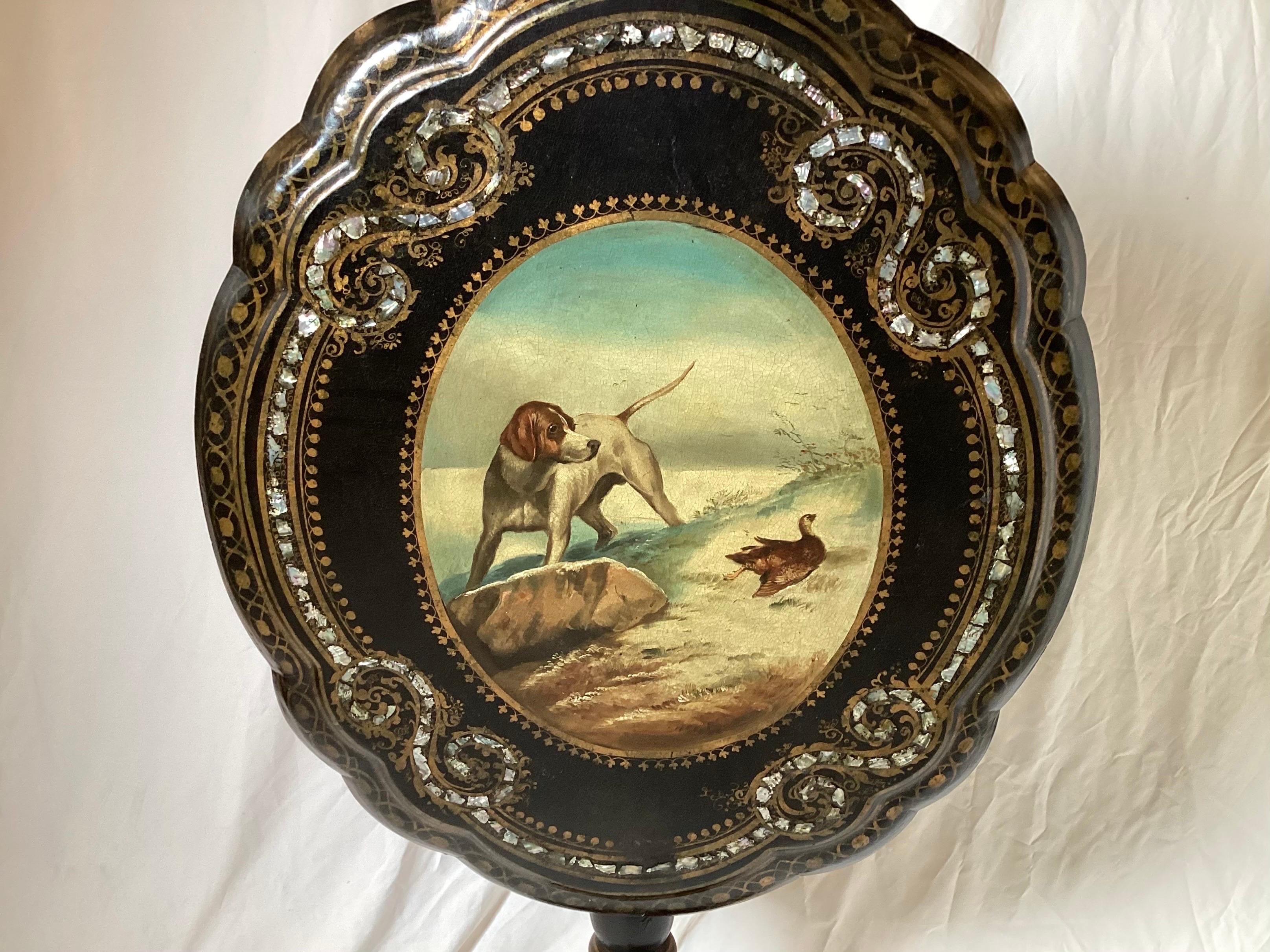An English shell inlaid, parcel gilt, paint decorated and ebonized papier mache tilt-top tea table, mid 19th century, the top centered by a scene depicting an English Pointer hunting dog pursuing a grouse.

Dimensions:height 23, width 28 deep 27
