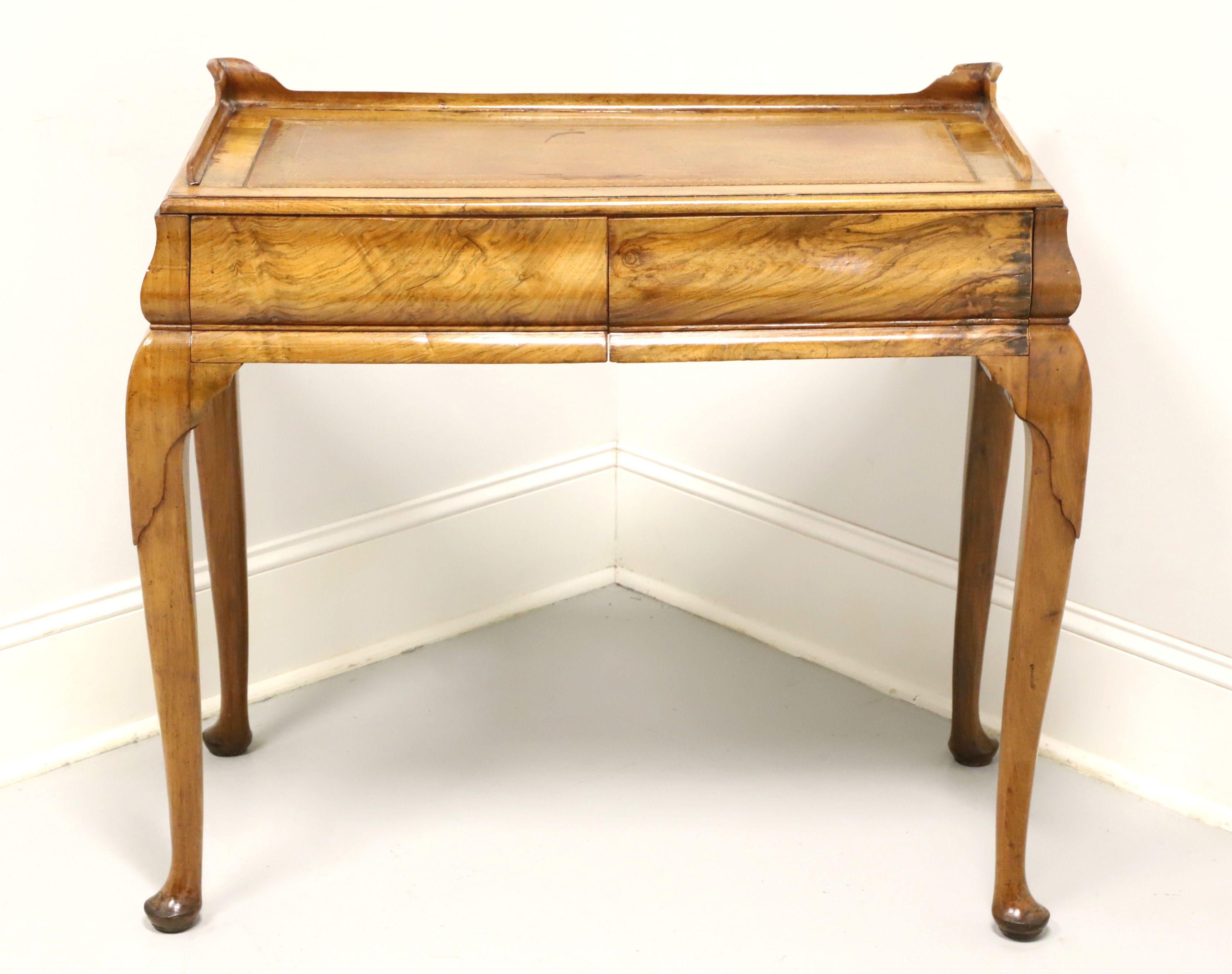 An antique Queen Anne style petite writing desk, unbranded. Solid hardwood, embossed leather top with carved low gallery, carved knees, cabriole legs and pad feet. Features two drawers of dovetail construction. Made in England, circa