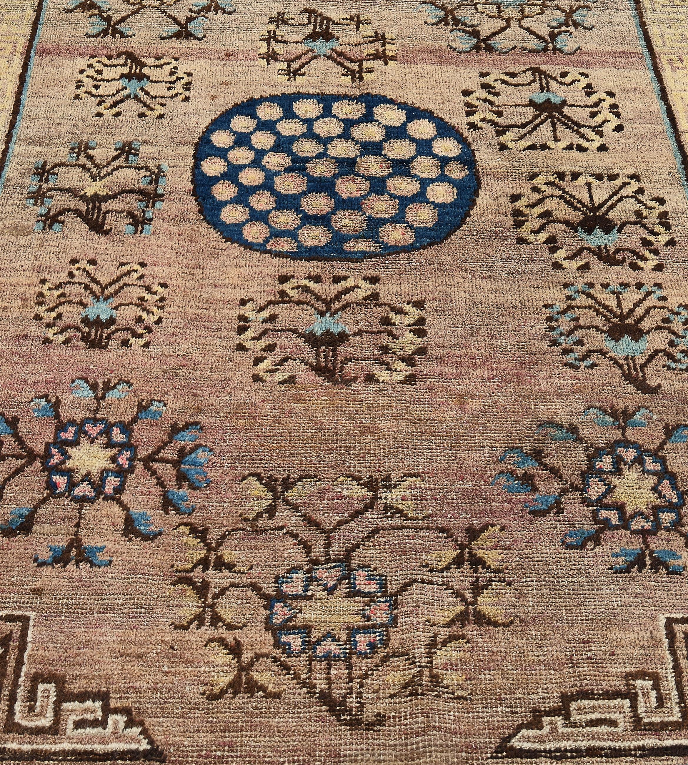 An antique, circa 1880, Khotan rug with a plum field with a central royal-blue roundel containing pomegranates surrounded by bold open floral sprays, the golden-yellow stepped spandrels, in a golden-yellow and dusty-pink key-pattern border, outer