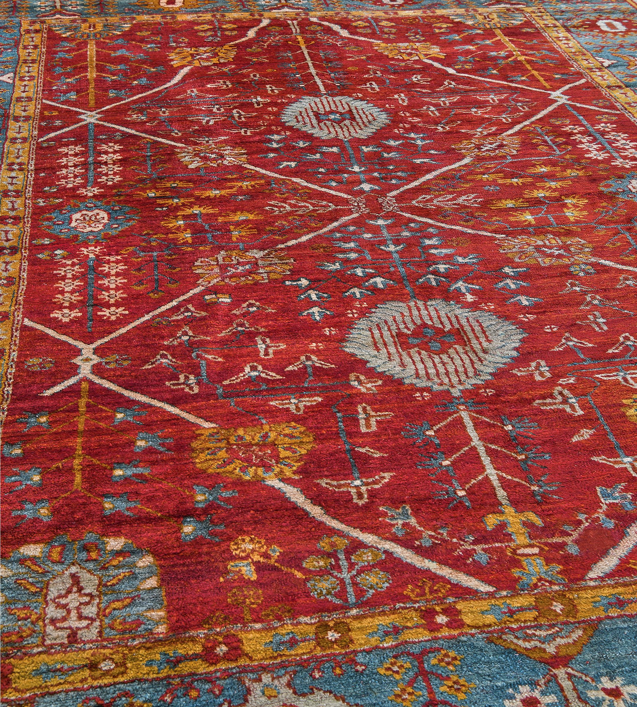 Dieser antike, um 1880 handgewebte anatolische Oushak-Teppich zeigt ein tomatenrotes Feld mit einem großen, elfenbeinfarbenen Gitter, das kühne Rauten bildet, die hellblaue, gezackte Rauten und himmelblaue, spitz zulaufende Rauten enthalten 