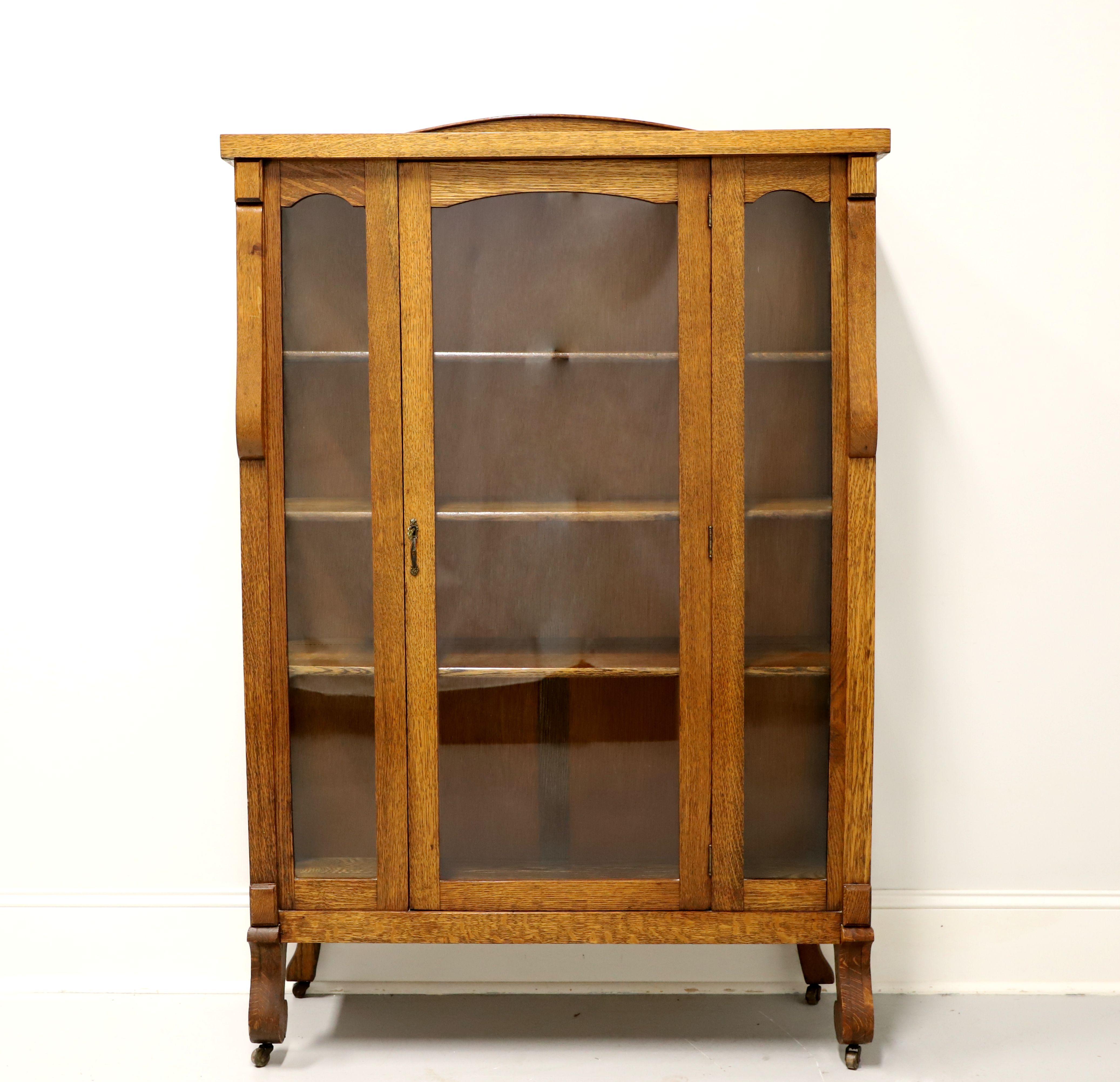 An antique Mission Arts & Crafts style china cabinet, unbranded. Solid tiger oak with brass hardware, low arched gallery to square edged top, decoratively carved accents to corners, one lockable center glass door door flanked by dual glass panels,