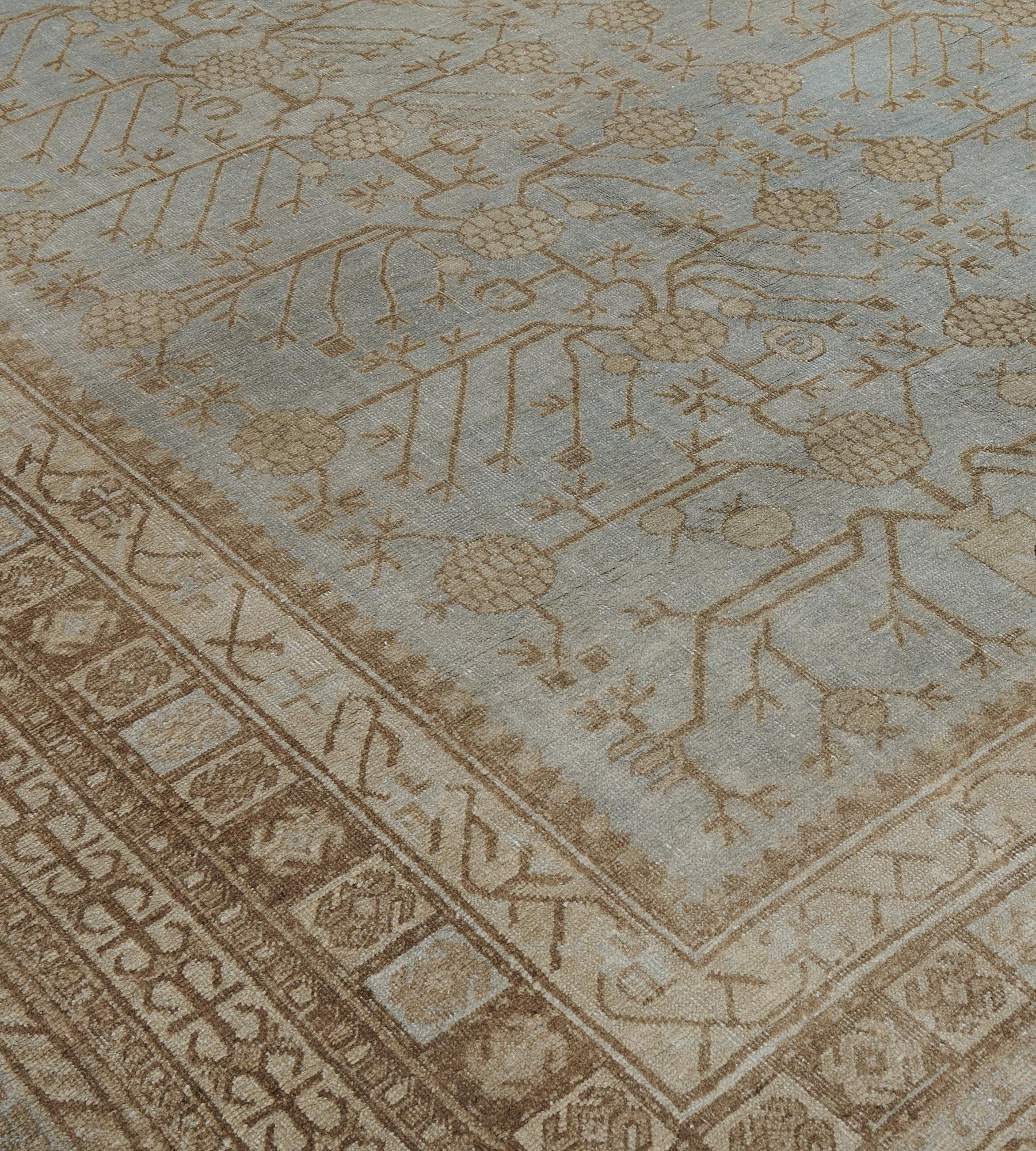 Ce tapis ancien du Khotan, datant de 1900, présente un champ bleu acier avec un motif général de vigne de grenade angulaire brun clair, dans une bordure jaune sable de vignes angulaires en crochet et en panneau, entre un panneau carré relié et des