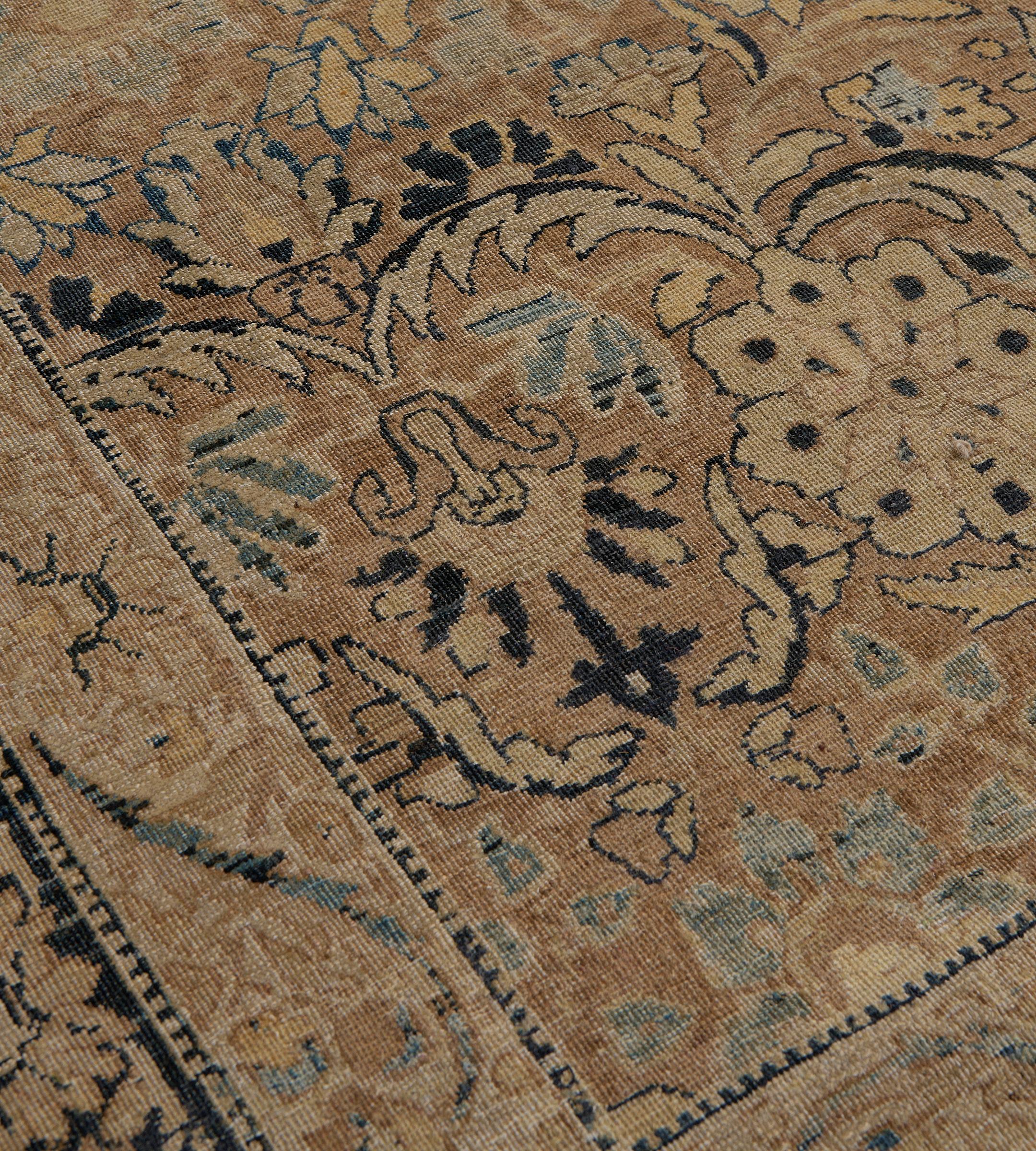 Questo antico tappeto persiano Kerman, risalente al 1900 circa, ha un campo marrone biscotto con un disegno generale di audaci palmette dorate che emettono foglie dentellate ricurve che collegano palmette blu chiaro e motivi floreali indaco intenso,