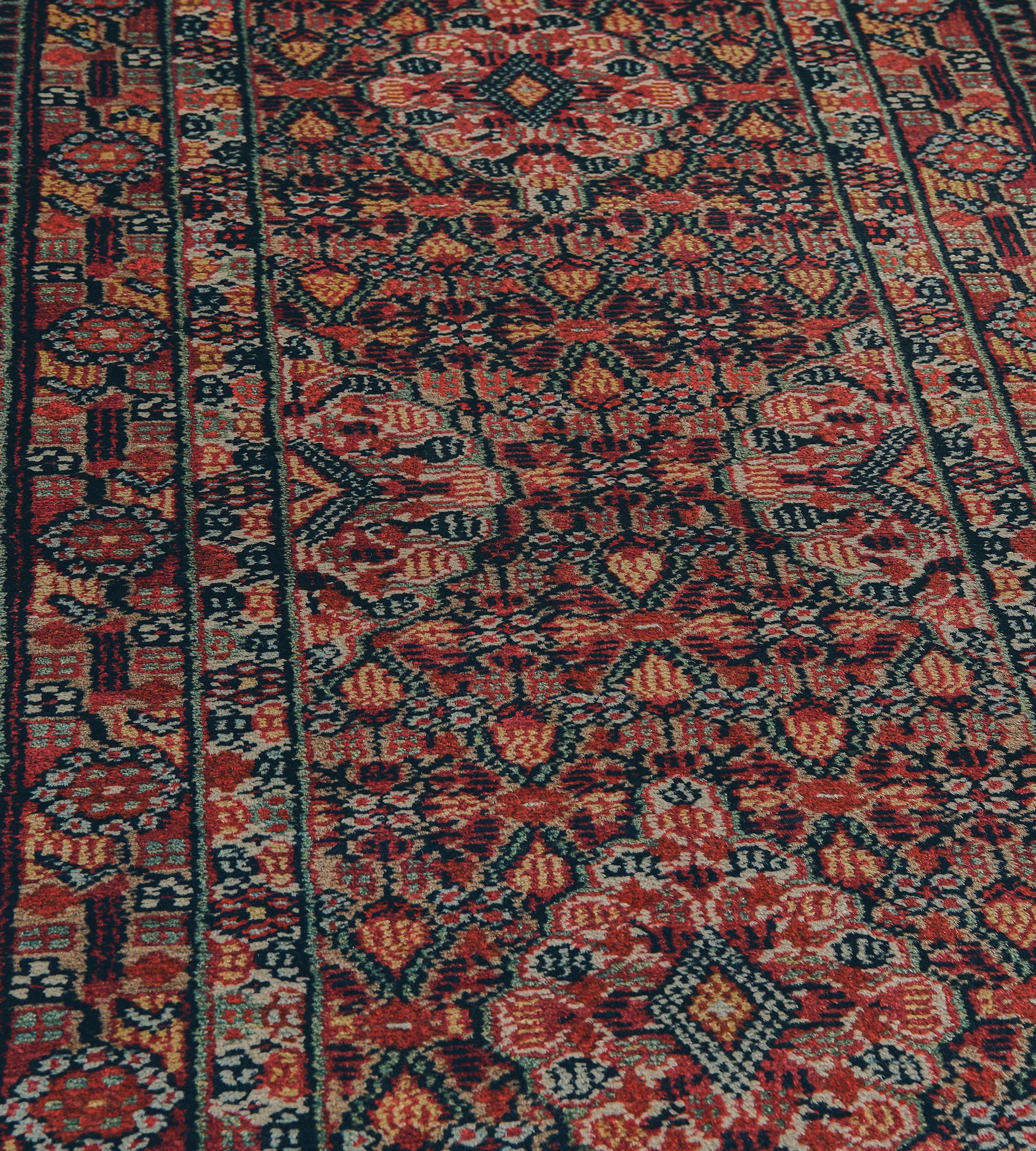 Questa antica passatoia persiana Serab, risalente al 1900 circa, presenta un campo marrone cammello con un disegno generale di motivi floreali angolari densi di colore rosso pomodoro, blu chiaro e giallo oro, circondati da losanghe laterali