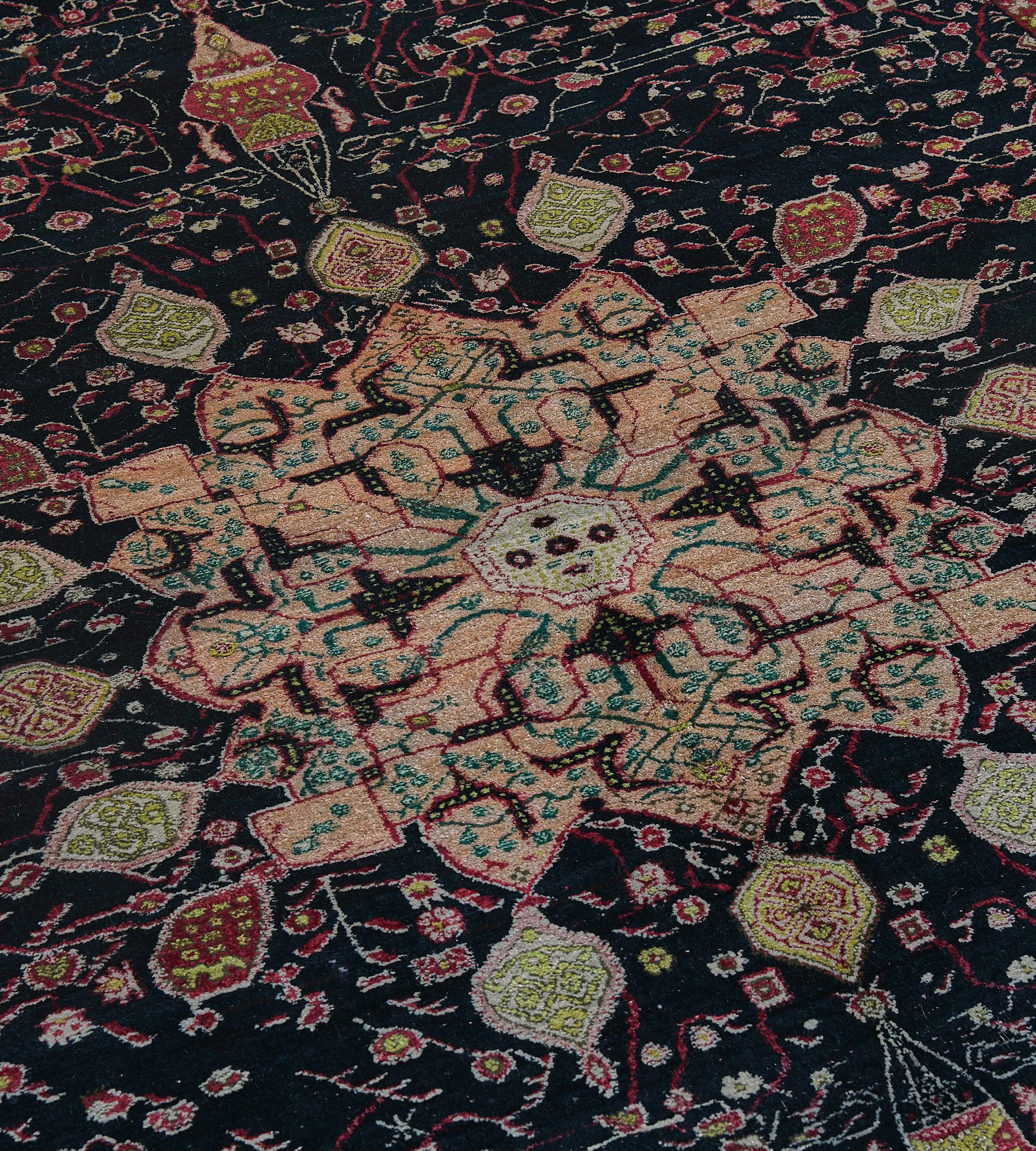 Dieser antike, um 1900, indische Agra-Teppich hat ein kohleschwarzes Feld mit einer zarten Blumenranke um ein zentrales weiches Terrakotta-Buckelmedaillon, das eine zentrale elfenbeinfarbene Raute enthält, die von einer kohleschwarzen, geteilten