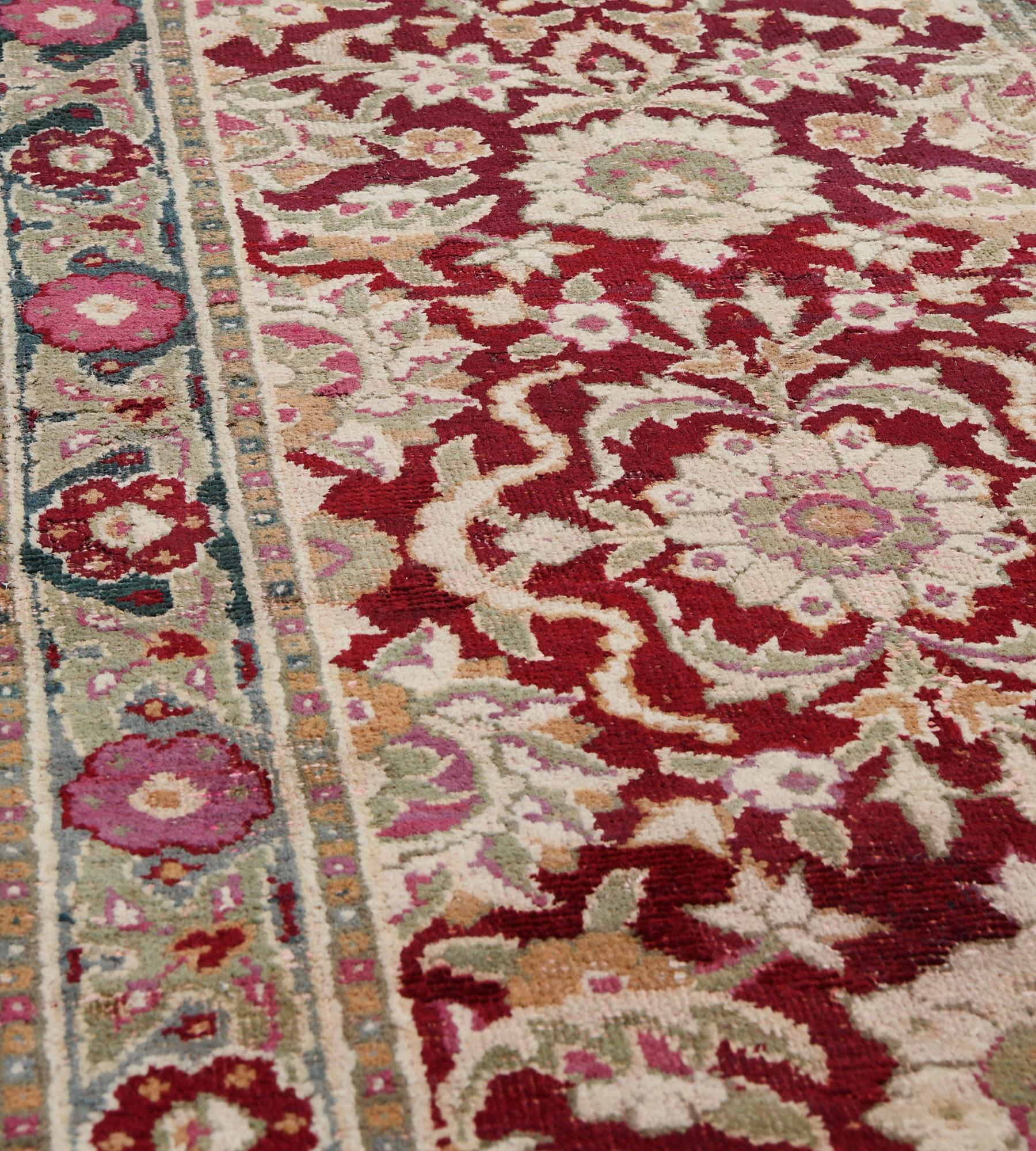 This antique, circa 1900, Agra runner has a deep red field with a central column of bold ivory, dusty-pink and moss-green palmette and scrolling floral vine flanked at each side with similar part palmettes, in a steel-blue border of deep red and