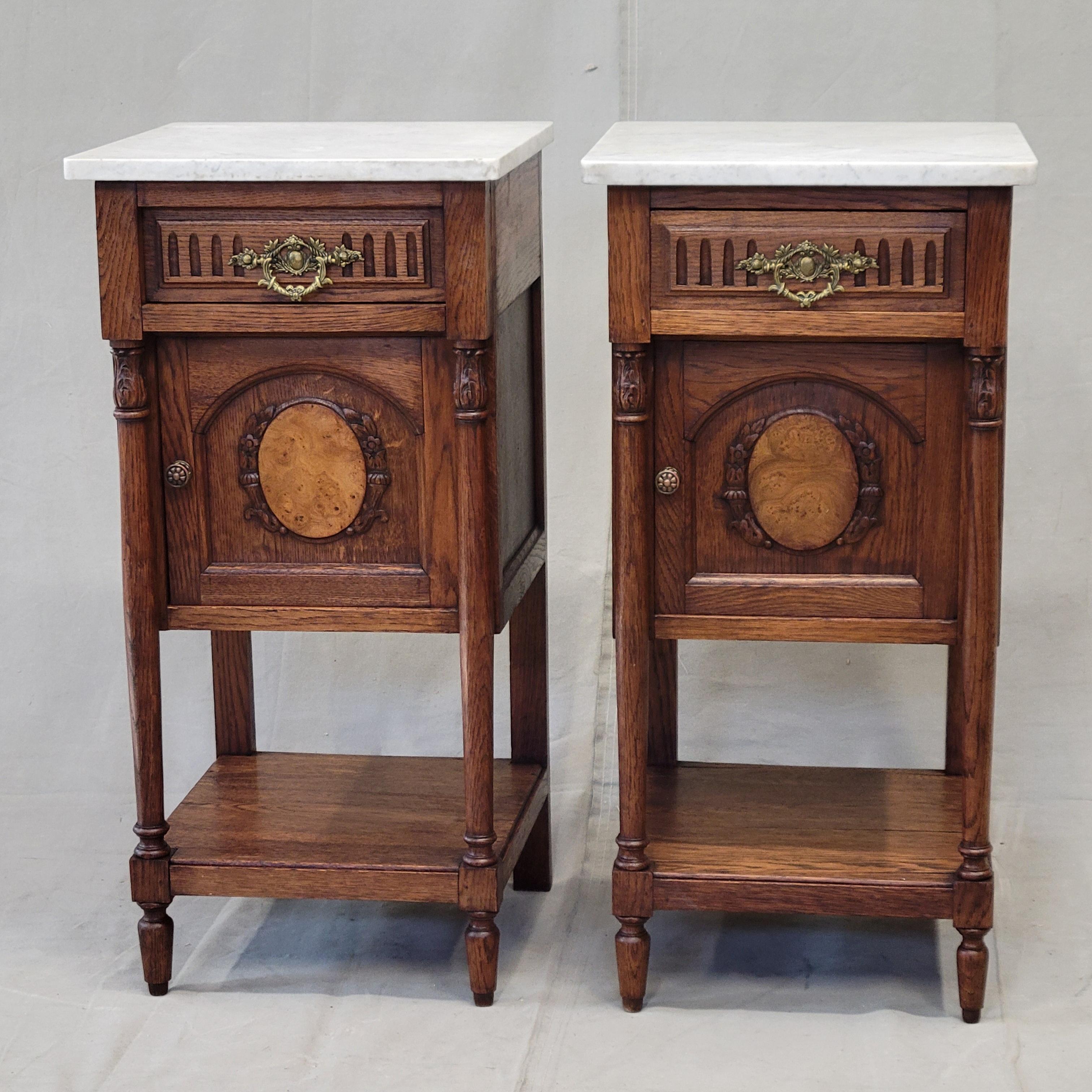 A gorgeous pair of early 1900s antique French oak nightstand pot cupboards with marble tops and original cast brass drawer pulls and door knobs. Notice the beautiful oval burl panel with carved surround in the center of each door. Marble is not
