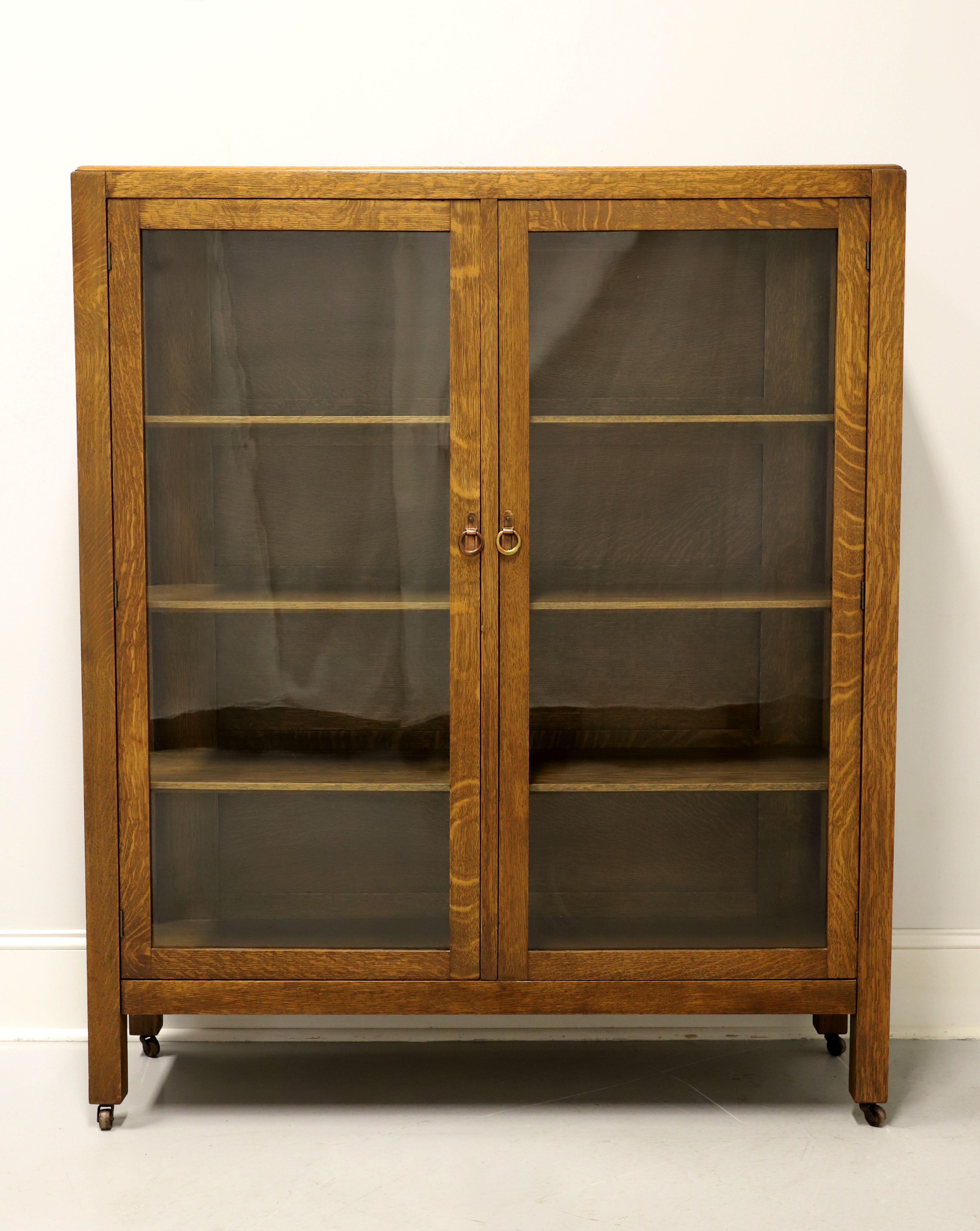 An antique Mission Arts & Crafts style china cabinet, unbranded. Solid tiger oak with brass hardware, two glass doors, glass side panels, square straight legs, and on brass casters. Features three adjustable plate grooved wooden shelves. Likely made