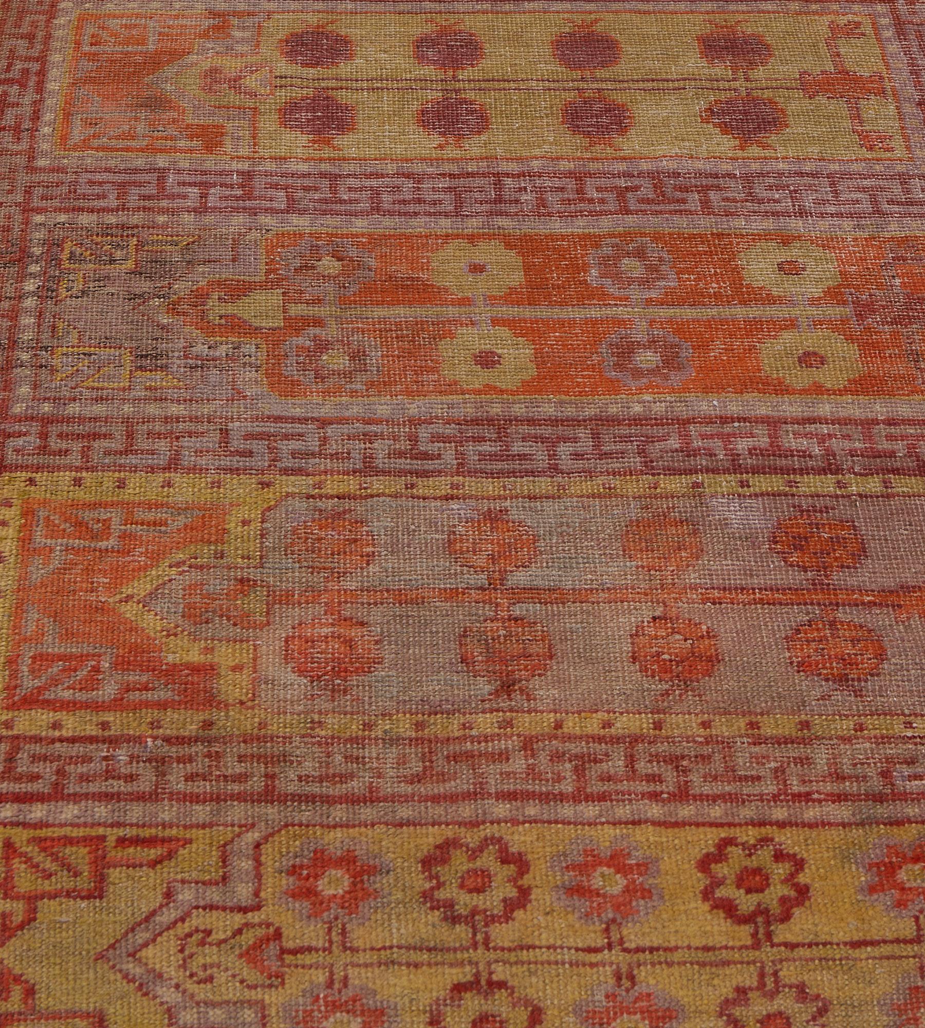 Questa antica passatoia di Khotan, risalente al 1900 circa, presenta un campo centrale con nove pannelli orizzontali policromi, ciascuno dei quali contiene un vaso che emette una vite floreale con un arco a gradini sovrastato da archi angolari con