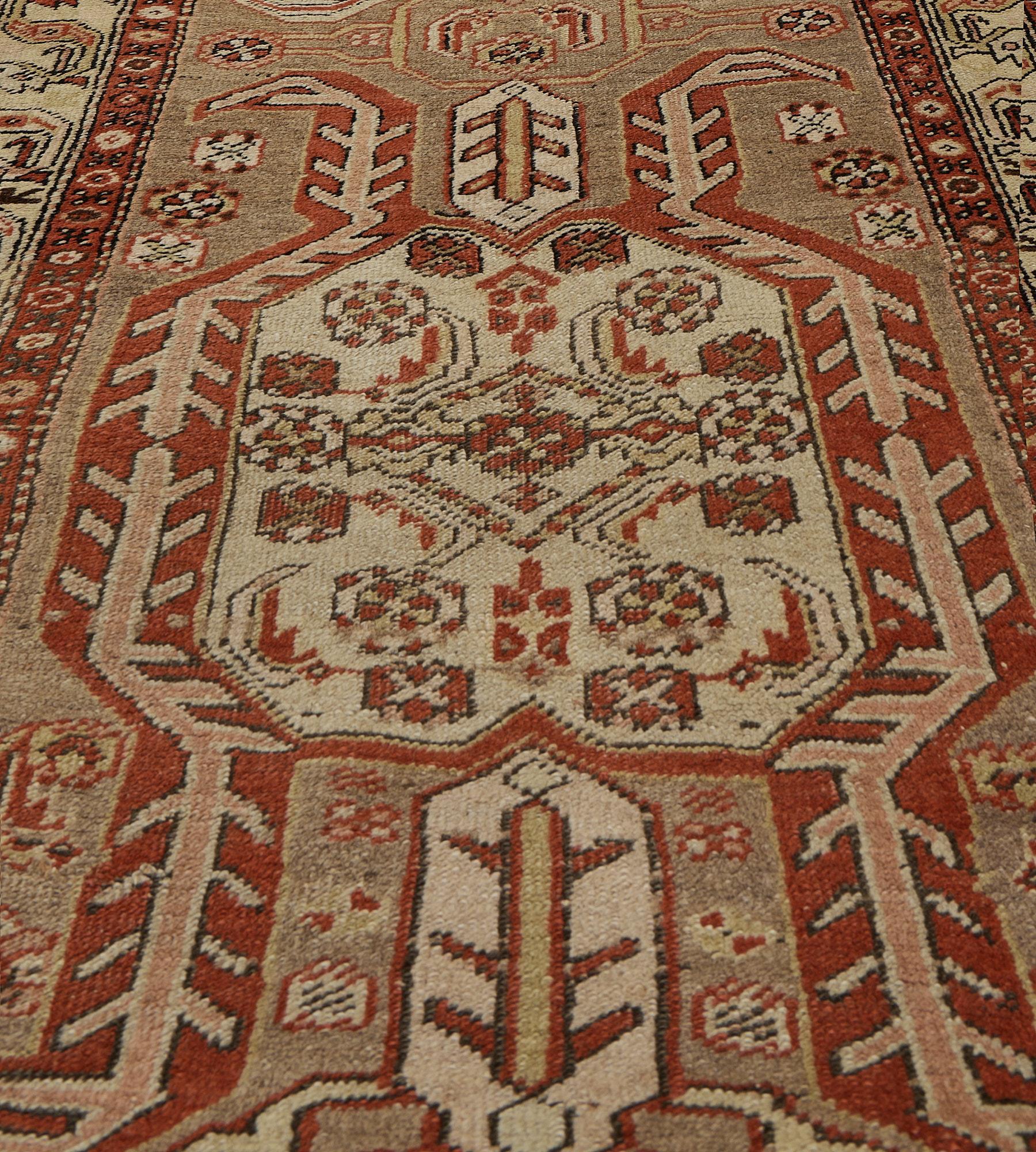 This antique, circa 1900, Heriz runner has a buff-brown field with a column of five bold octagon polychrome lozenges edged by angular hooked stripes with a stylised bird motif within the band above and below, the centre with an angular floral and