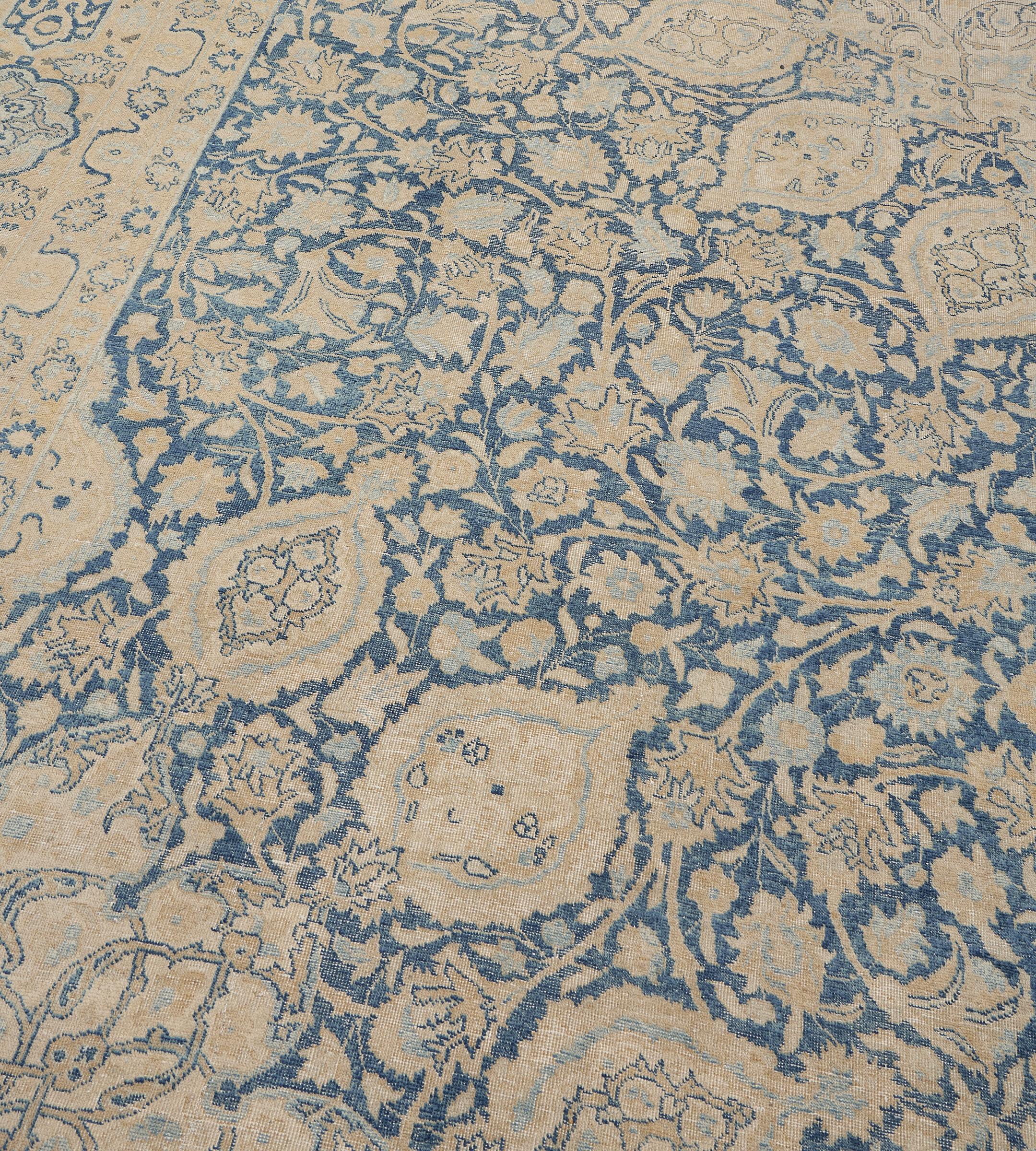 Questo tappeto Tabriz antico, del 1900 circa, ha un campo azzurro con una fitta palmetta e una foglia di colore giallo sabbia, azzurro e avorio che si muovono intorno a un grande medaglione centrale di colore simile con una vite arabescata e teste
