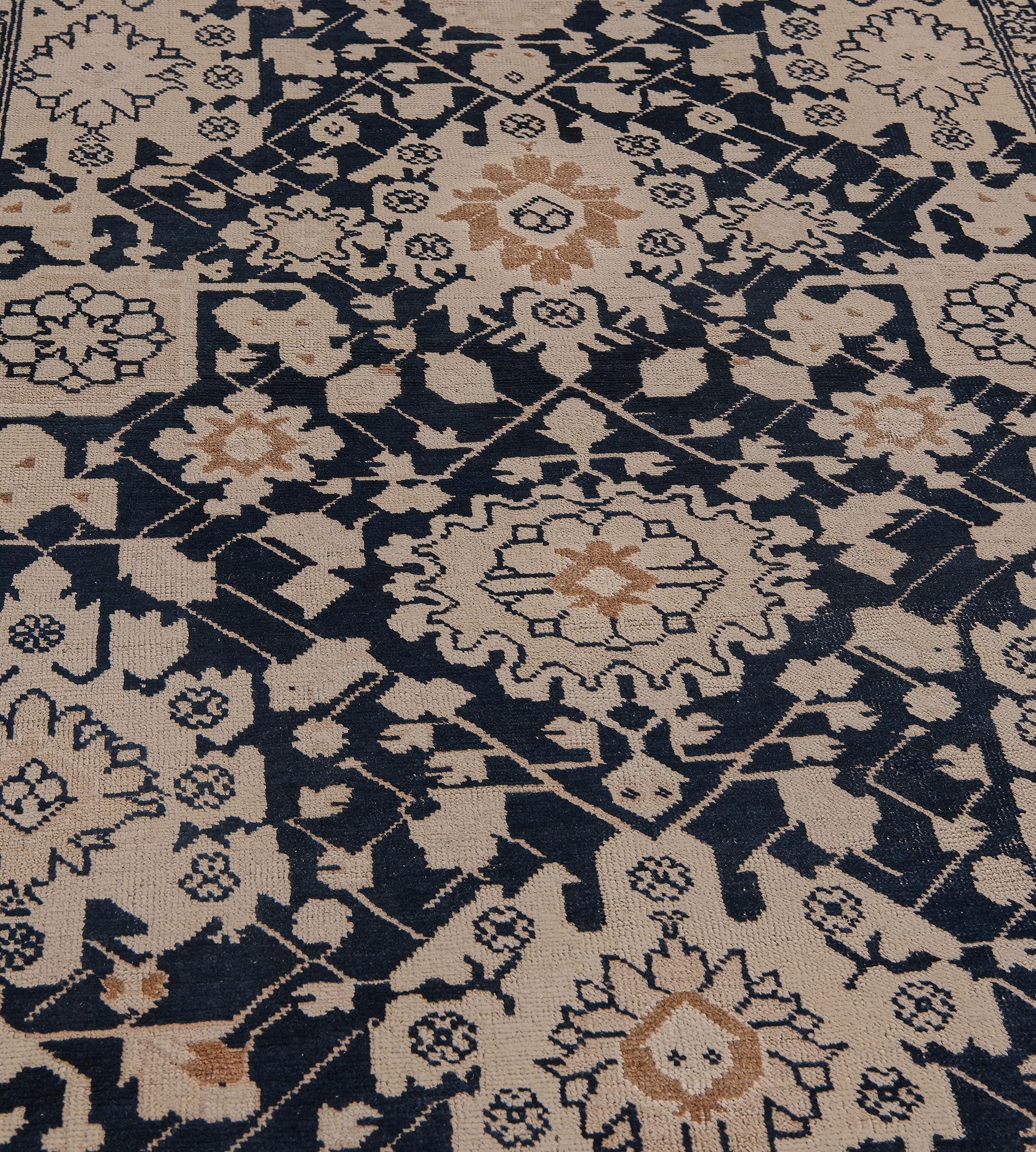 Ce chemin de table antique, datant d'environ 1900, présente un champ anthracite-indigo avec un motif général de palmettes angulaires, de fleurs et de vignes feuillues brun chamois, brun renard et bleu ciel, dans une étroite bordure brun chamois avec
