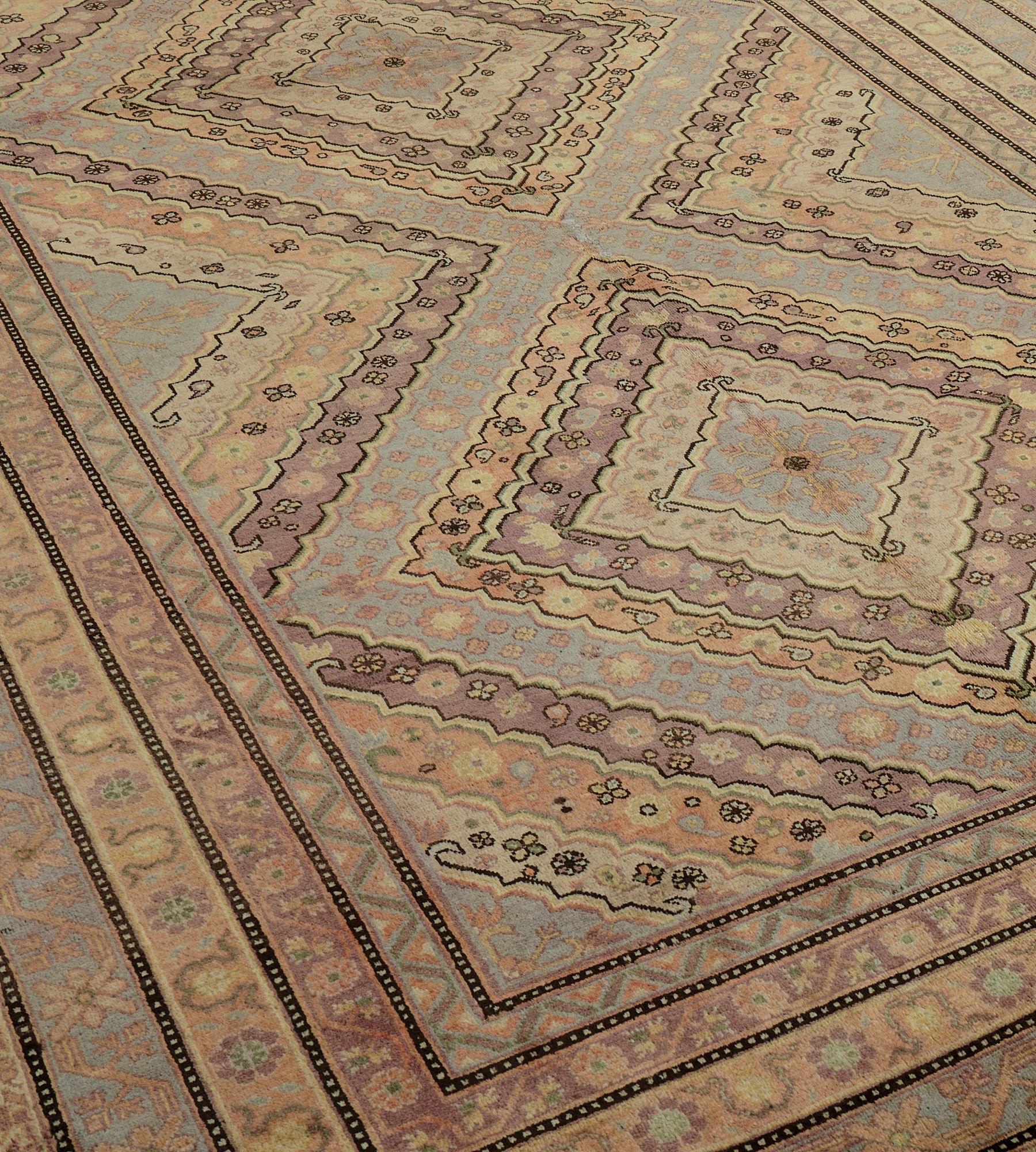 This antique, circa 1900, Khotan rug features a field with three lozenge medallions each with a central light grey-blue lozenge surrounded by plum, sandy-yellow and buff-brown stripes containing floral motifs surrounded by a light grey-blue similar