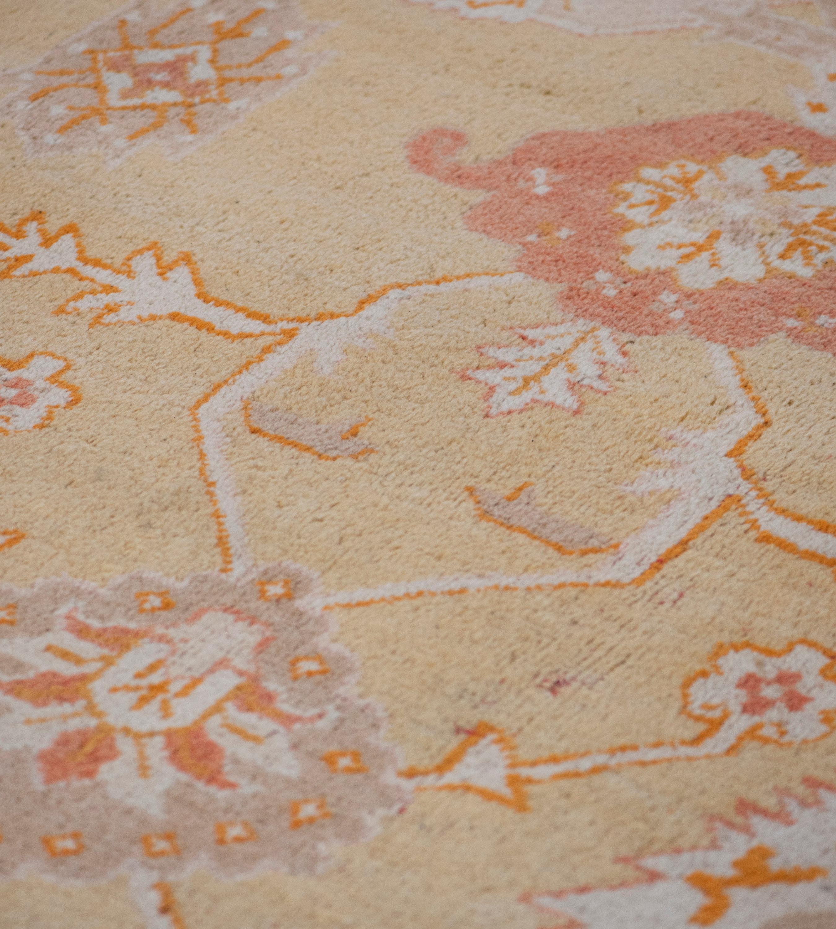 This antique, circa 1900, Oushak rug has a soft-yellow field with angular terracotta-red and ivory floral vine around a lozenge medallion with a central flowerhead issuing bold terracotta-red palmettes and scattered with further flowerheads, the