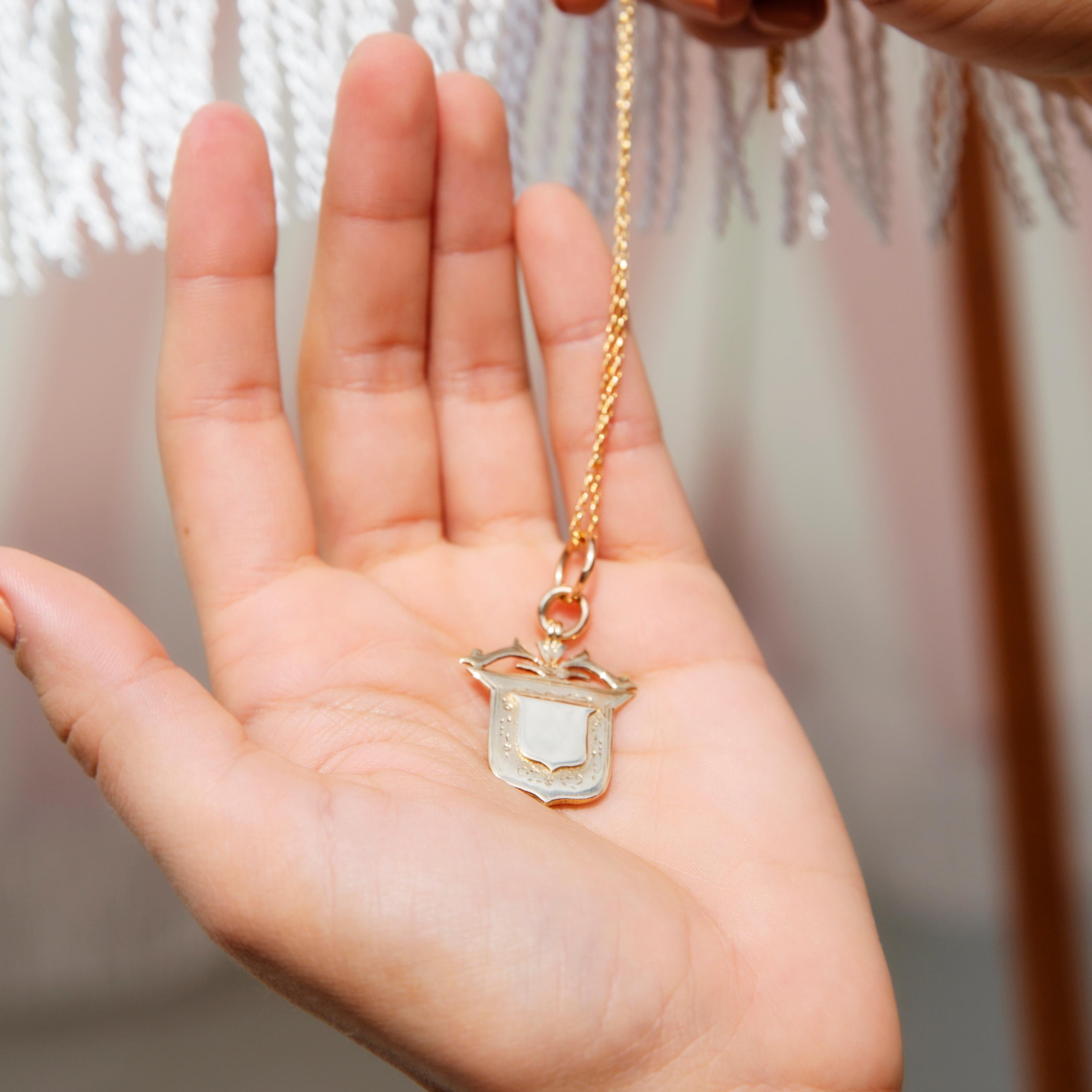 Crafted in 9 carat yellow gold, this charming vintage antique pendant features a central shield motif on a shield-shaped platform, evoking feelings of peace and protection. The Mawlsley Pendant is comfortably worn below the neck and against the