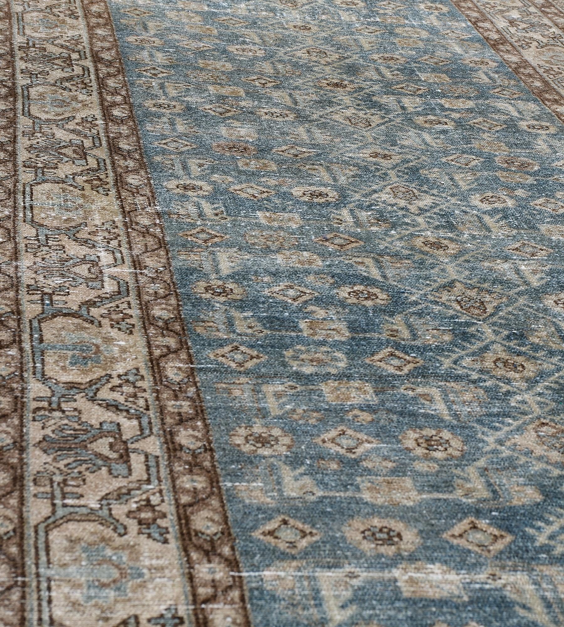 This antique, circa 1910, Malayer runner has a shaded light blue field with an overall design of angular herati-pattern, in a buff-brown angular light blue and shaded brown palmette and floral vine border between shaded brown meandering floral vine