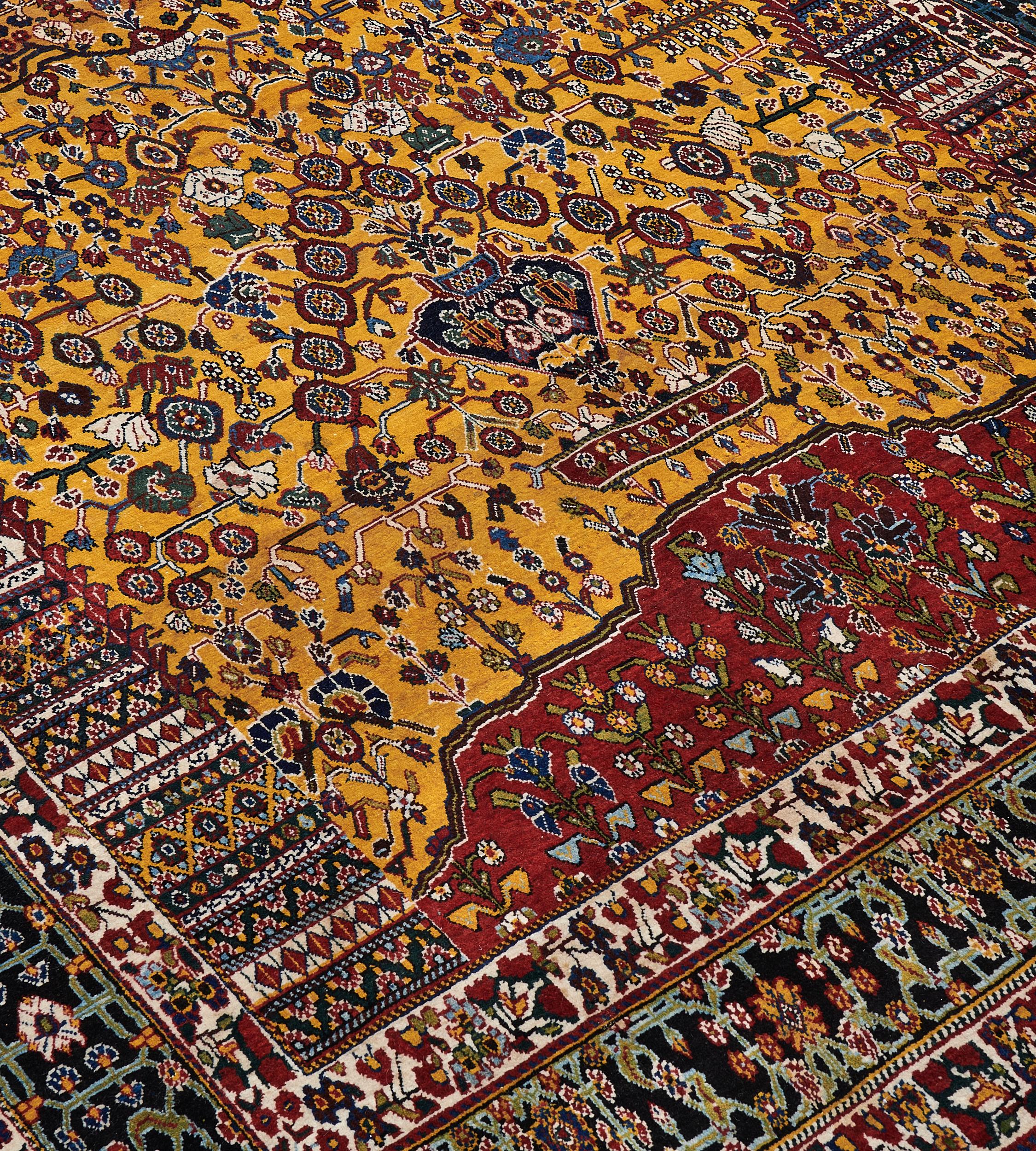 This antique, circa 1910, Qashqai prayer rug has a field with a golden-yellow field containing a dense profusion of angular flowering vine issuing from a blue vase which is supported by a small fox-brown floral panel, a fox-brown curved mound below